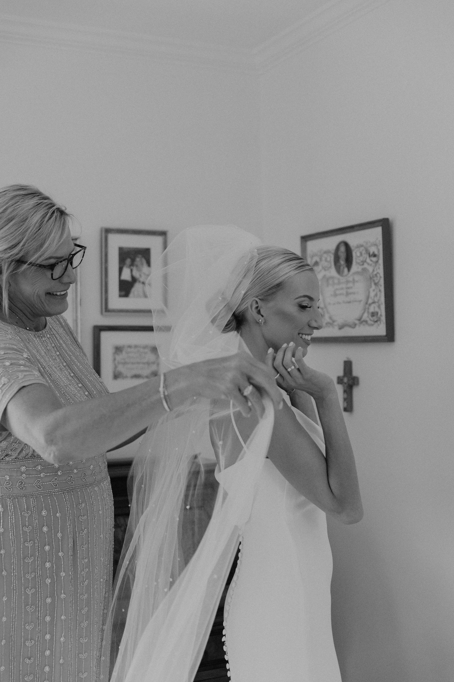 Black and white photo of wedding preparation with veil adjustments.