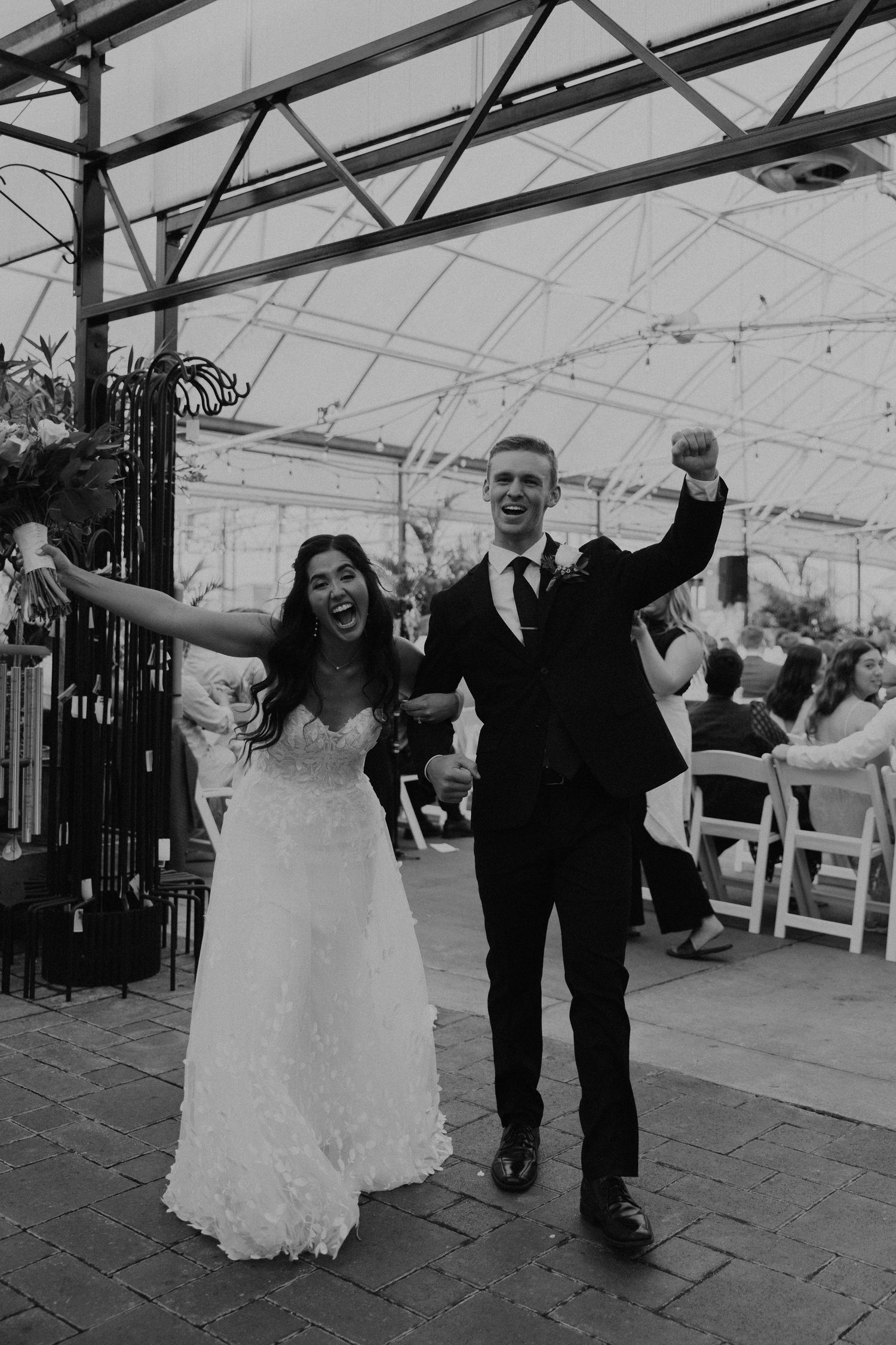 Joyful wedding couple celebrates while walking down the aisle in a greenhouse venue.