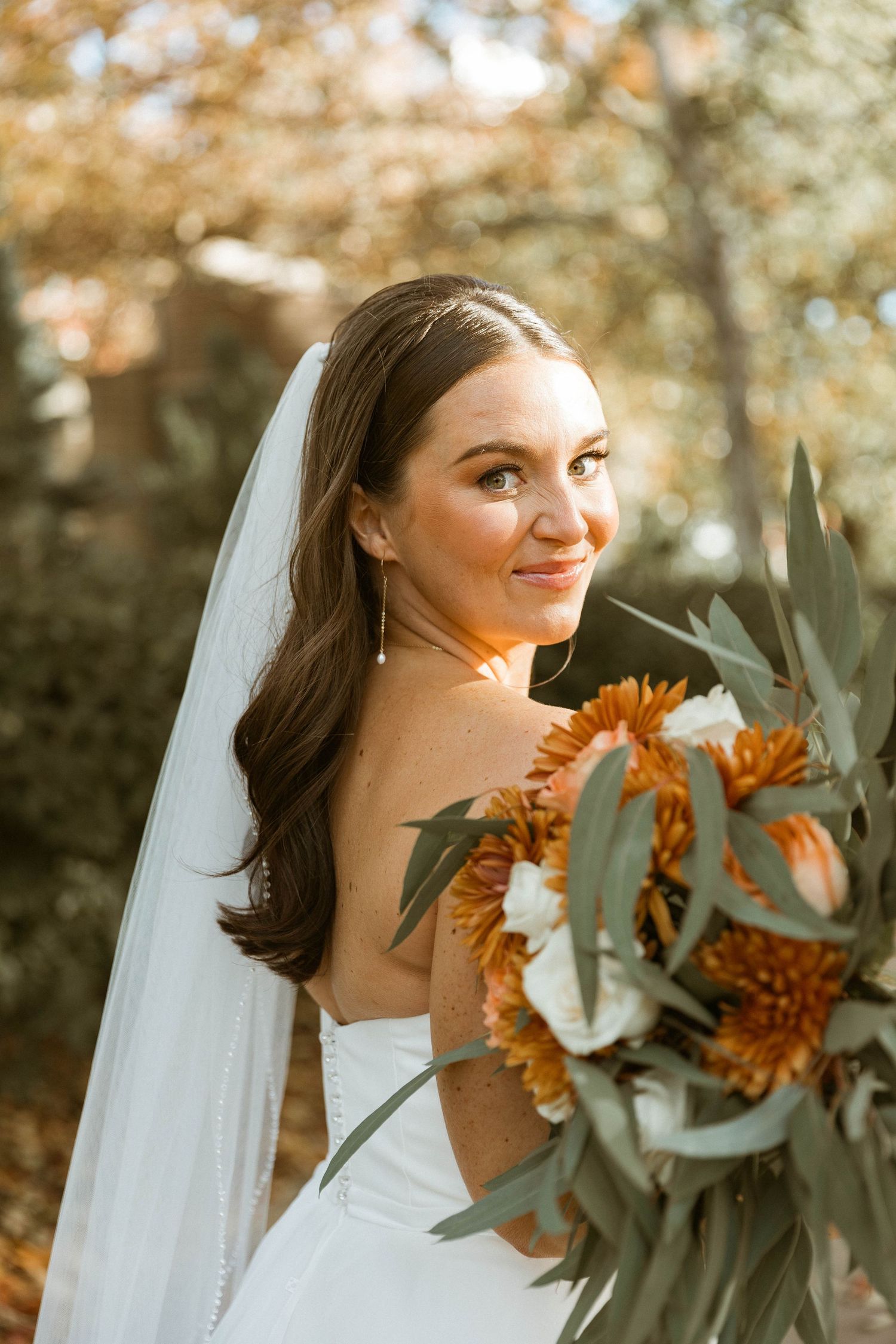 Autumn wedding bouquet in warm orange tones complementing outdoor bridal portrait.