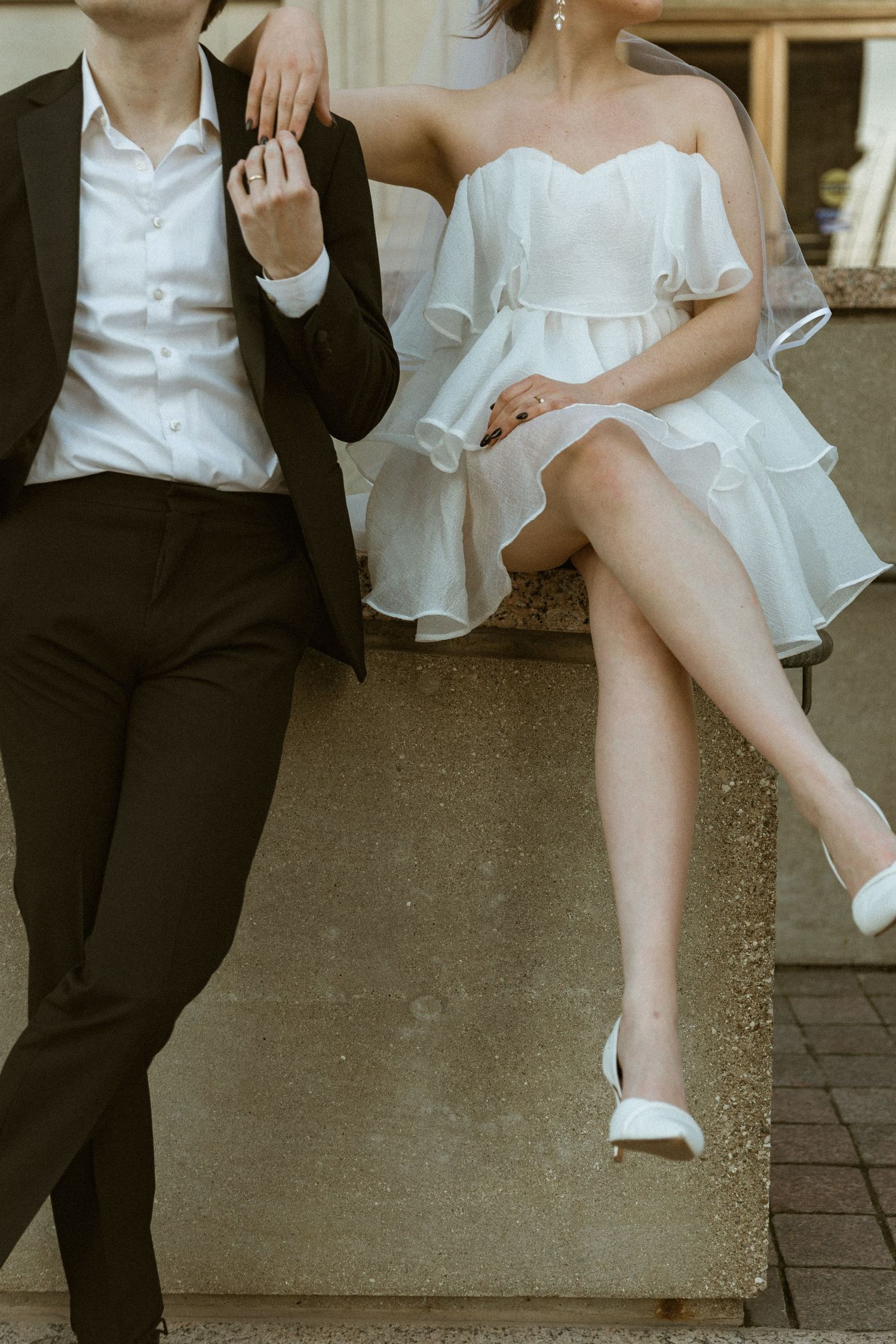 Wedding couple sitting on stone steps in elegant black and white attire showing close up details of their outfits.