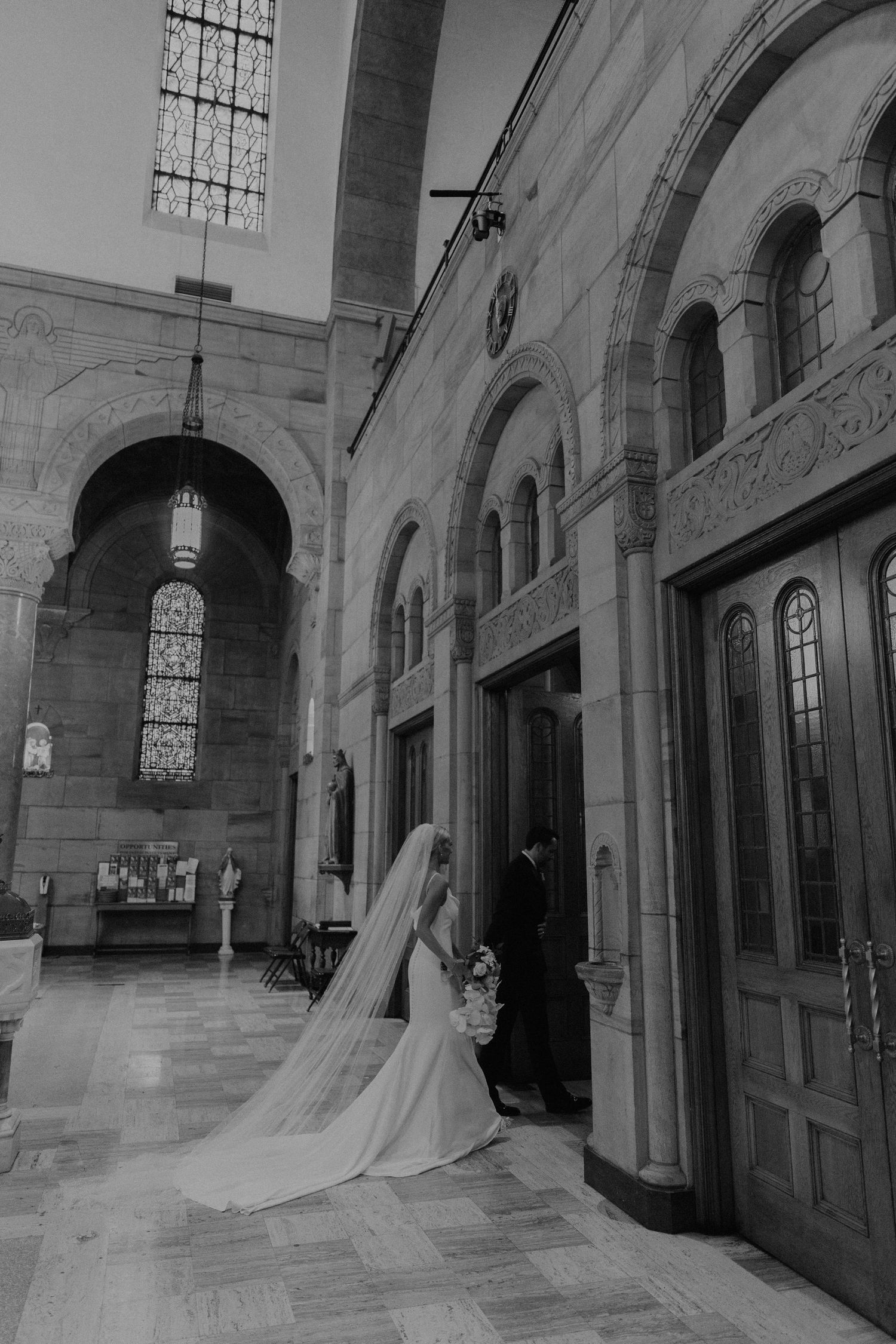 Black and white photo of a cathedral hallway with a long flowing wedding dress and veil.