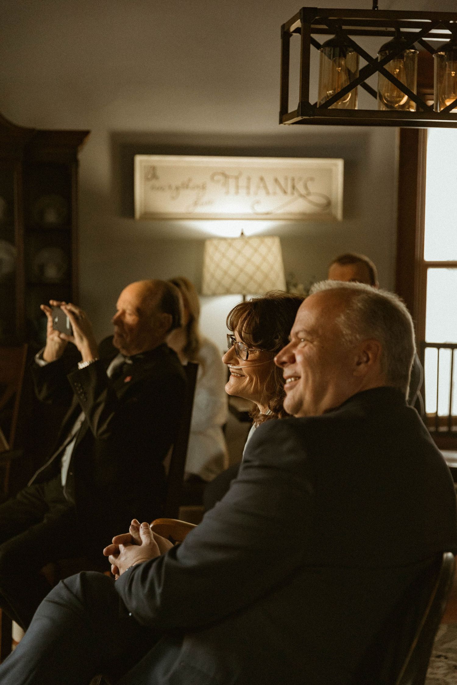 A group of guests laughing together in a cozy living room with a 'Thanks' sign visible in the background.