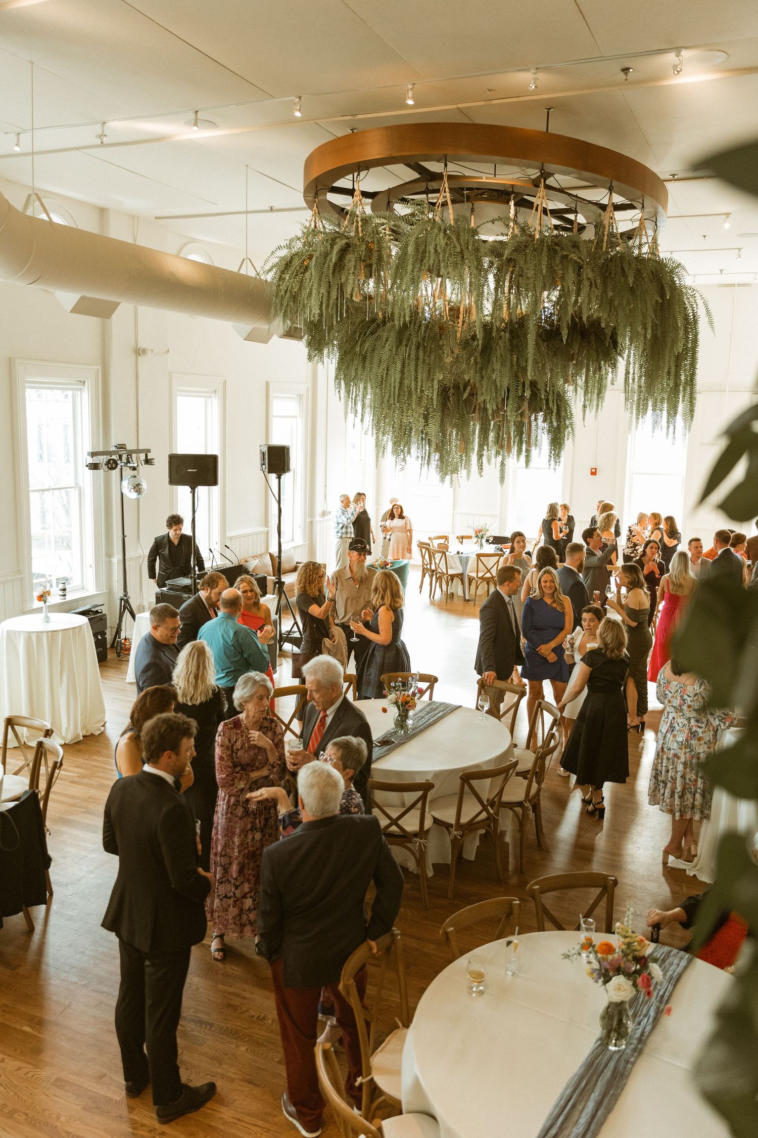 Reception gathering in an elegant venue with suspended moss decor and guests mingling.