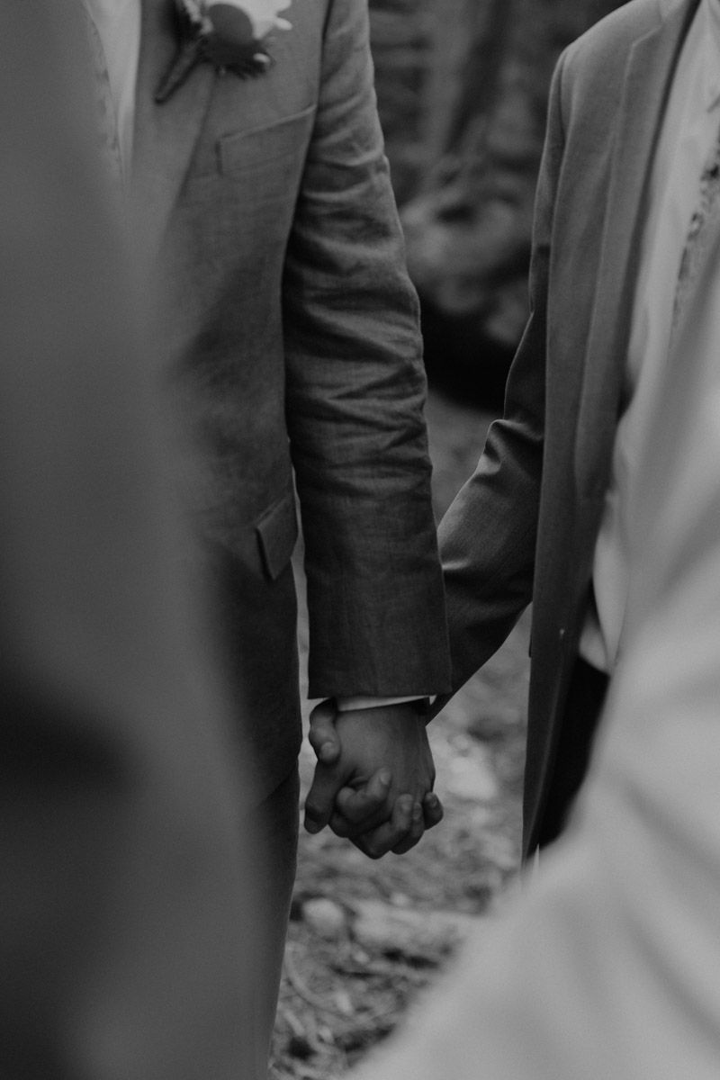 Close-up black and white photo of two hands clasped together while wearing formal suits.