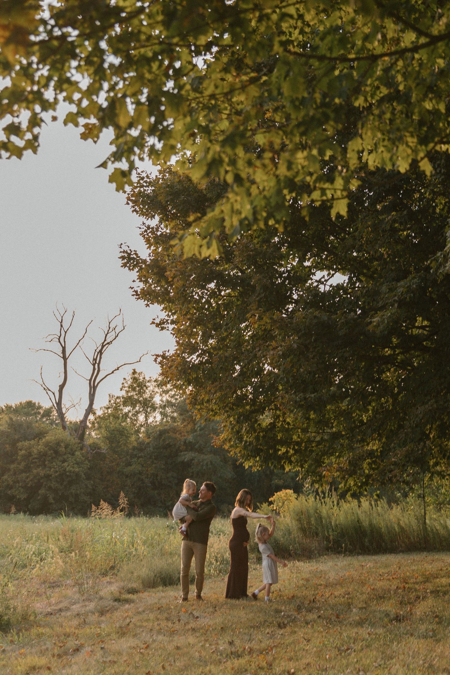 A group of people stand together in a grassy field at sunset with golden autumn foliage in the background.