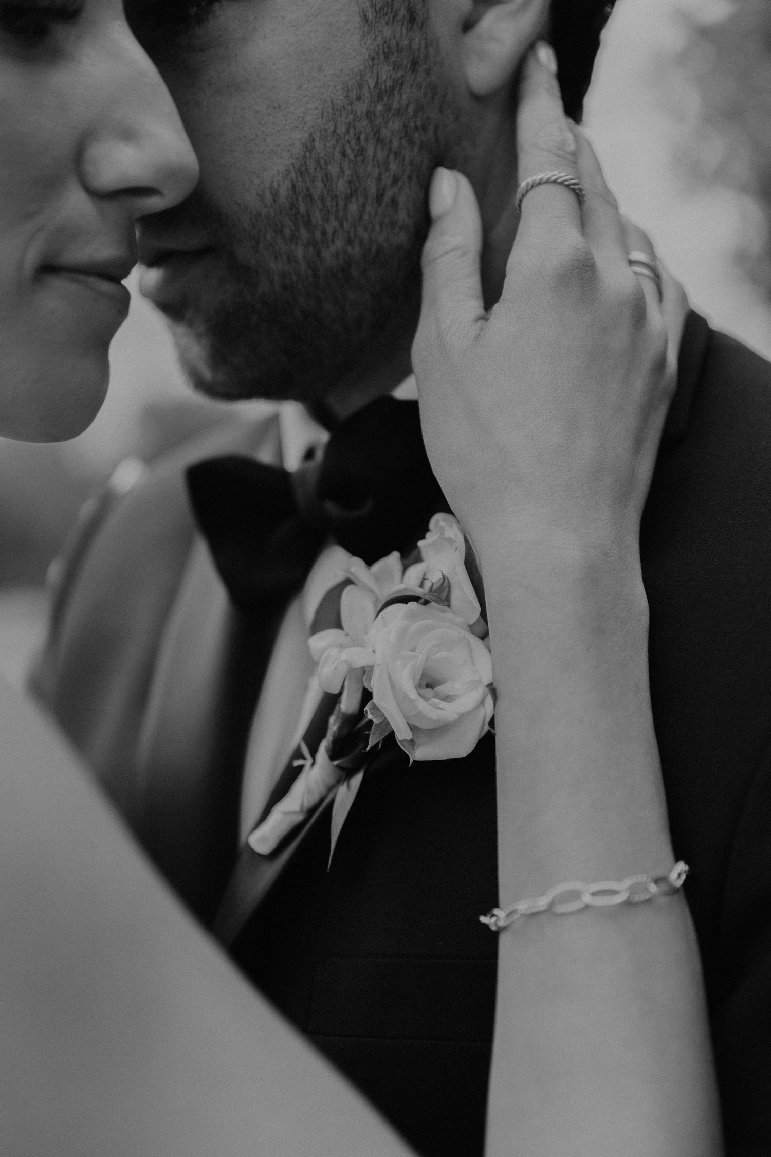 Black and white close-up of romantic moment with boutonniere and jewelry details.