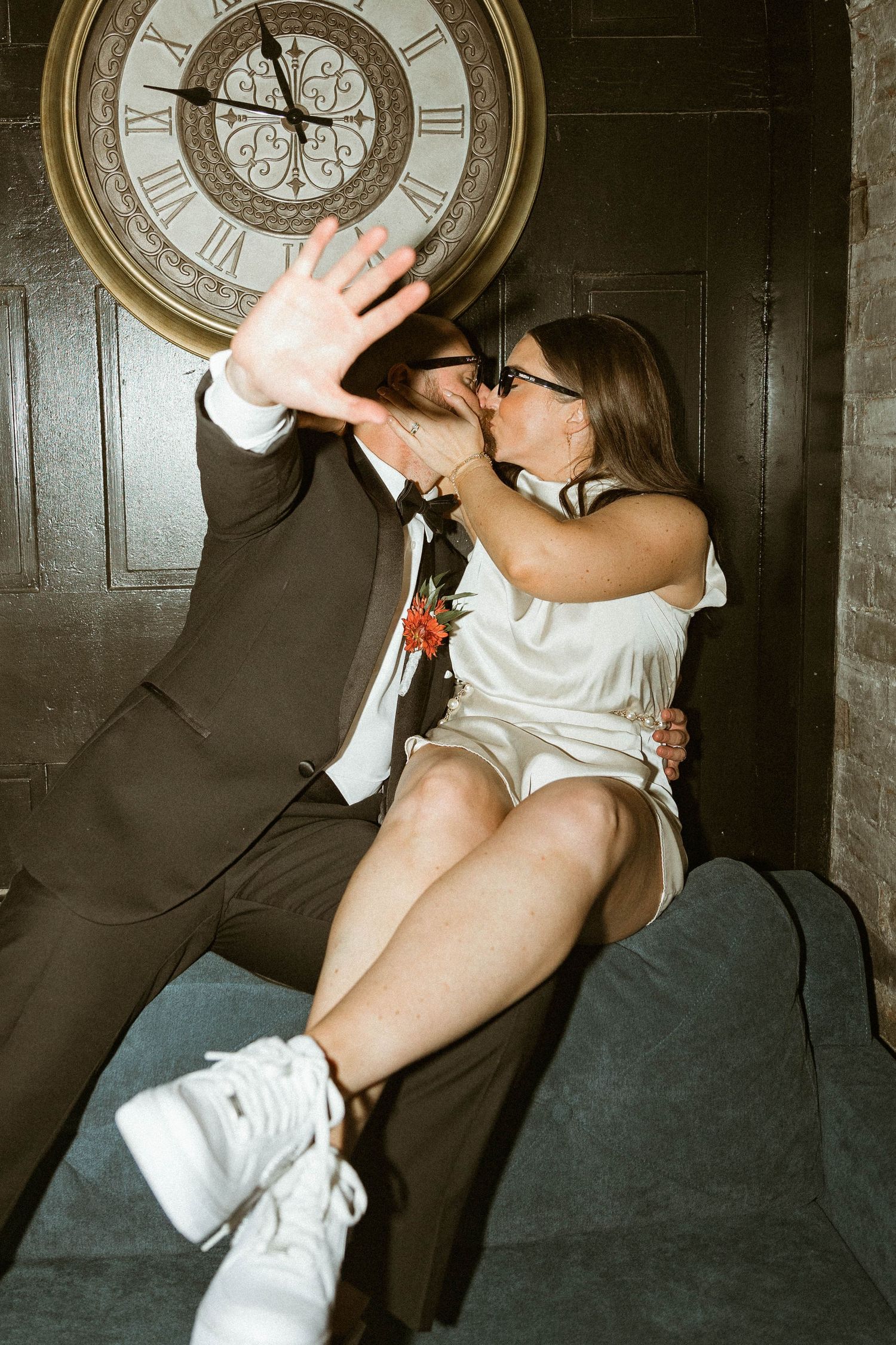 A romantic moment captured under an antique clock during a wedding celebration.