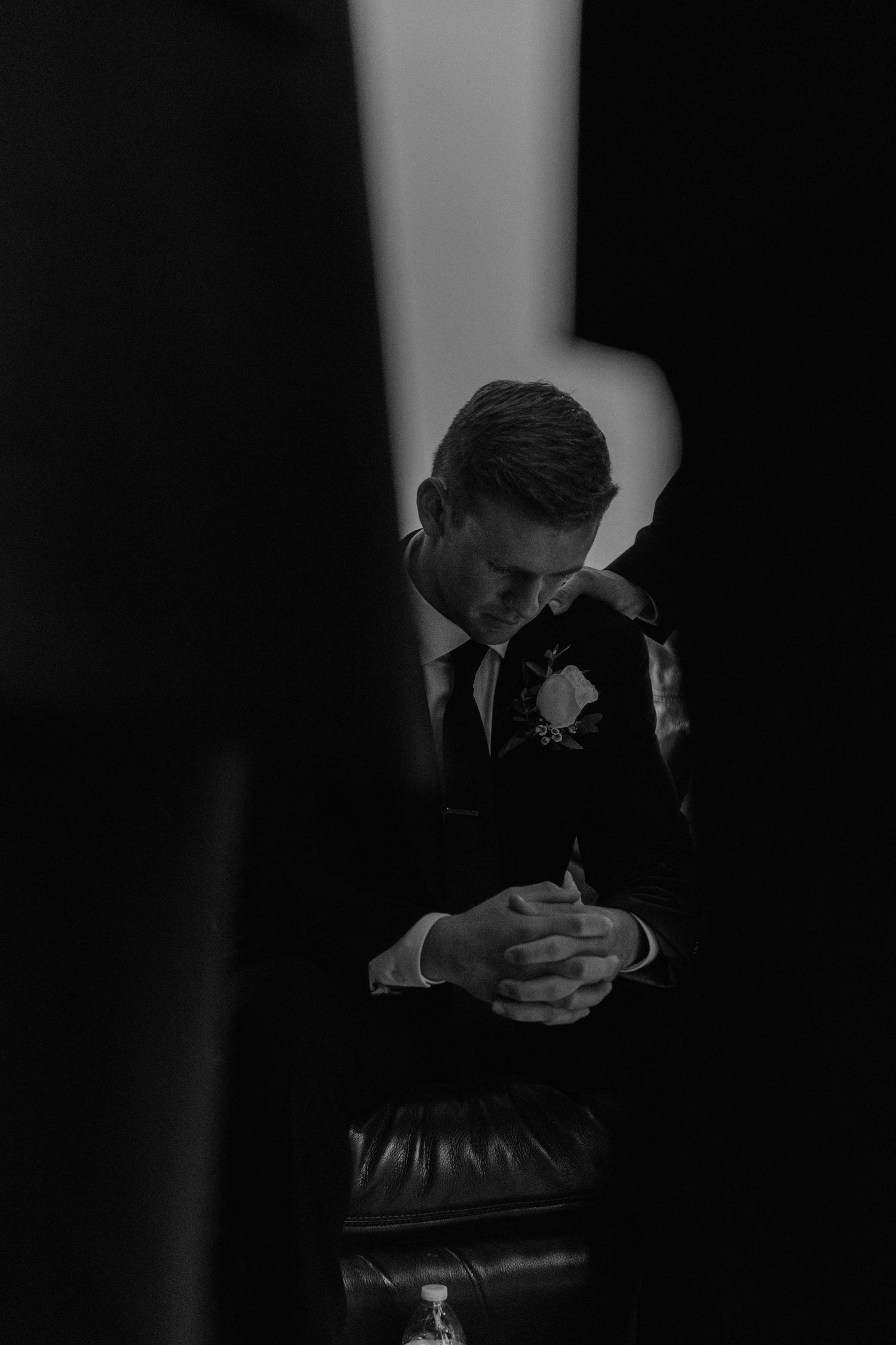 Dramatic black and white portrait in low light showing formal wedding attire details.
