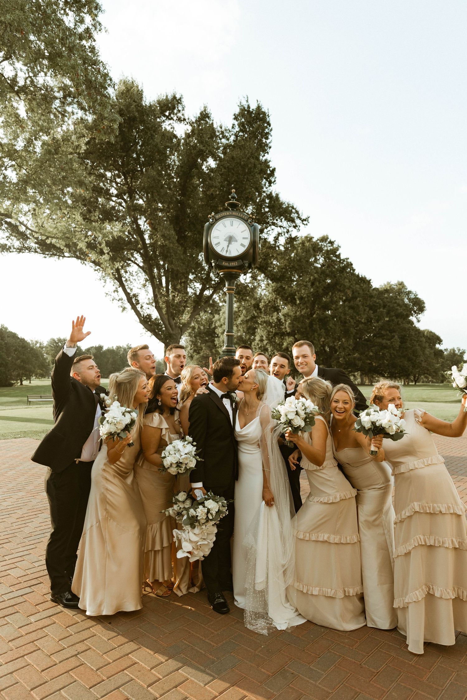 Wedding party in blush pink dresses and formal attire posing outdoors for fun group photos.