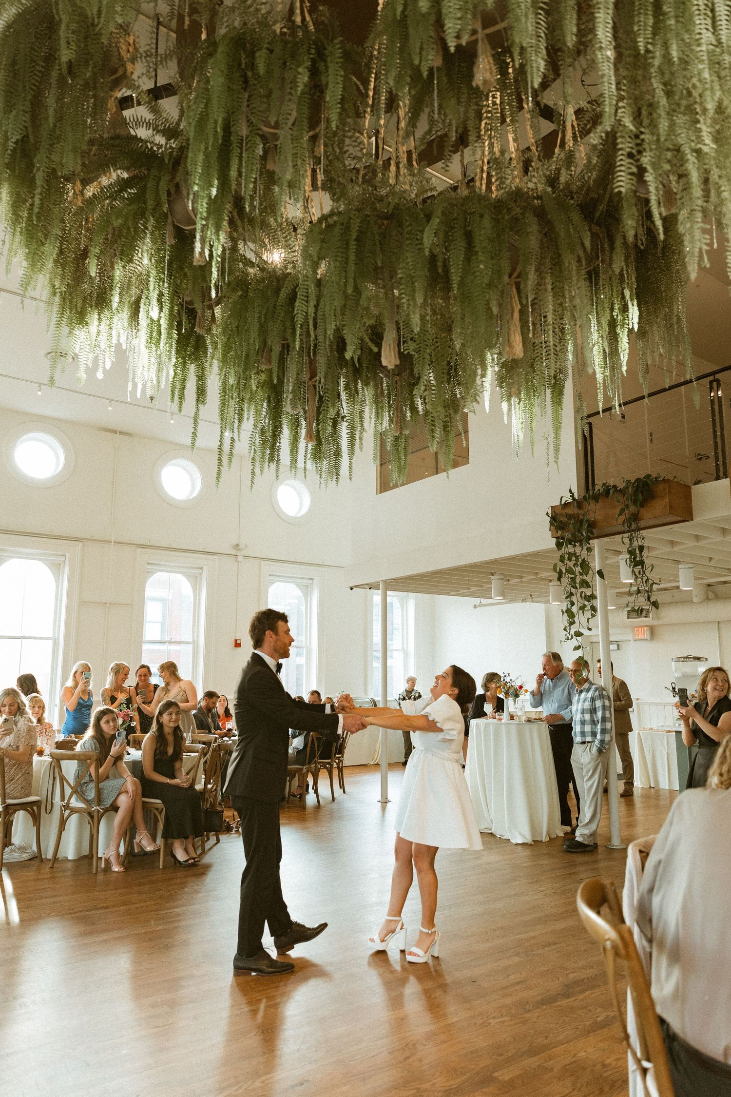A wedding celebration in a modern venue with hanging greenery and string lights.