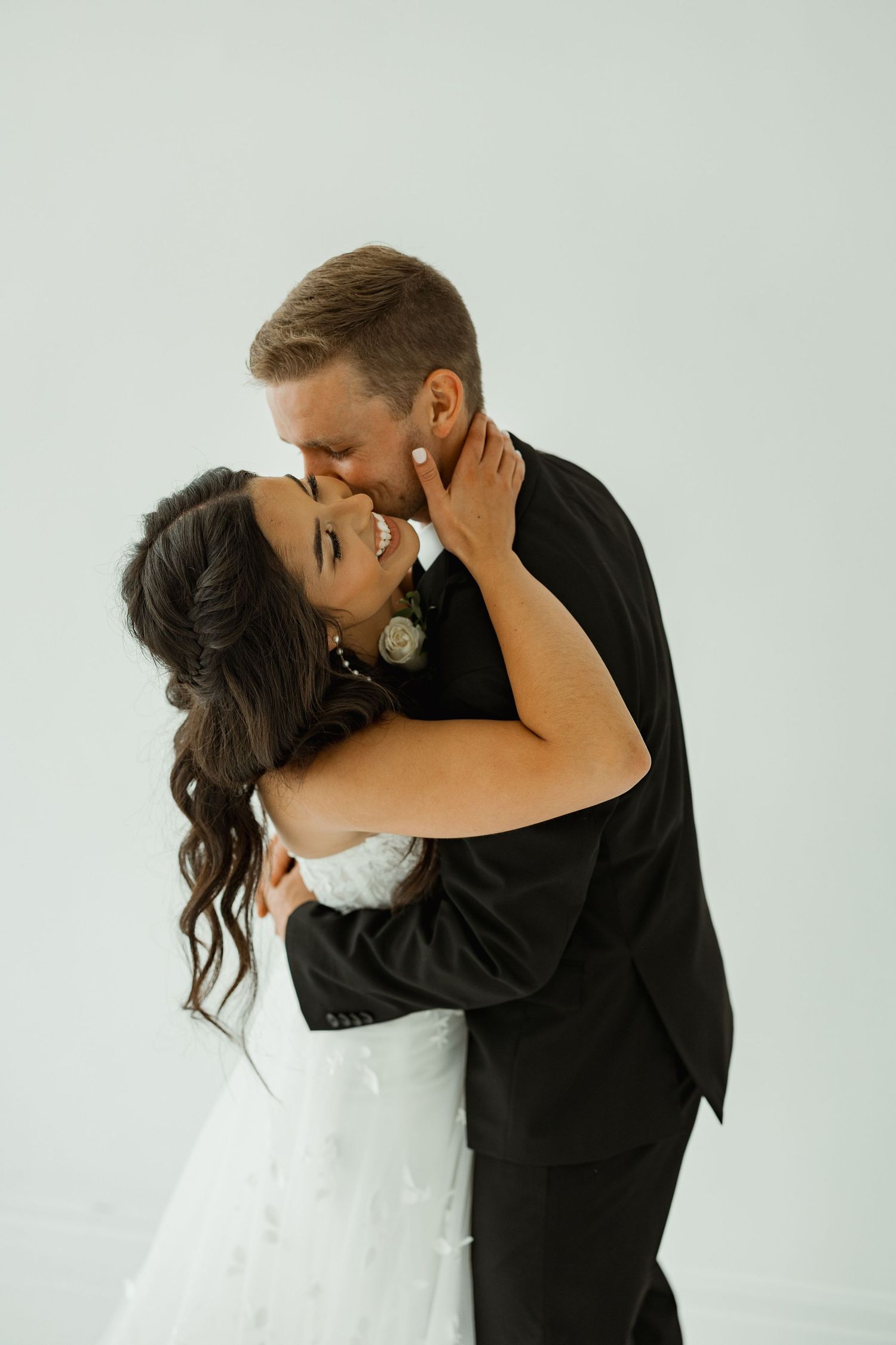 An intimate moment between newlyweds embracing against a white studio backdrop.