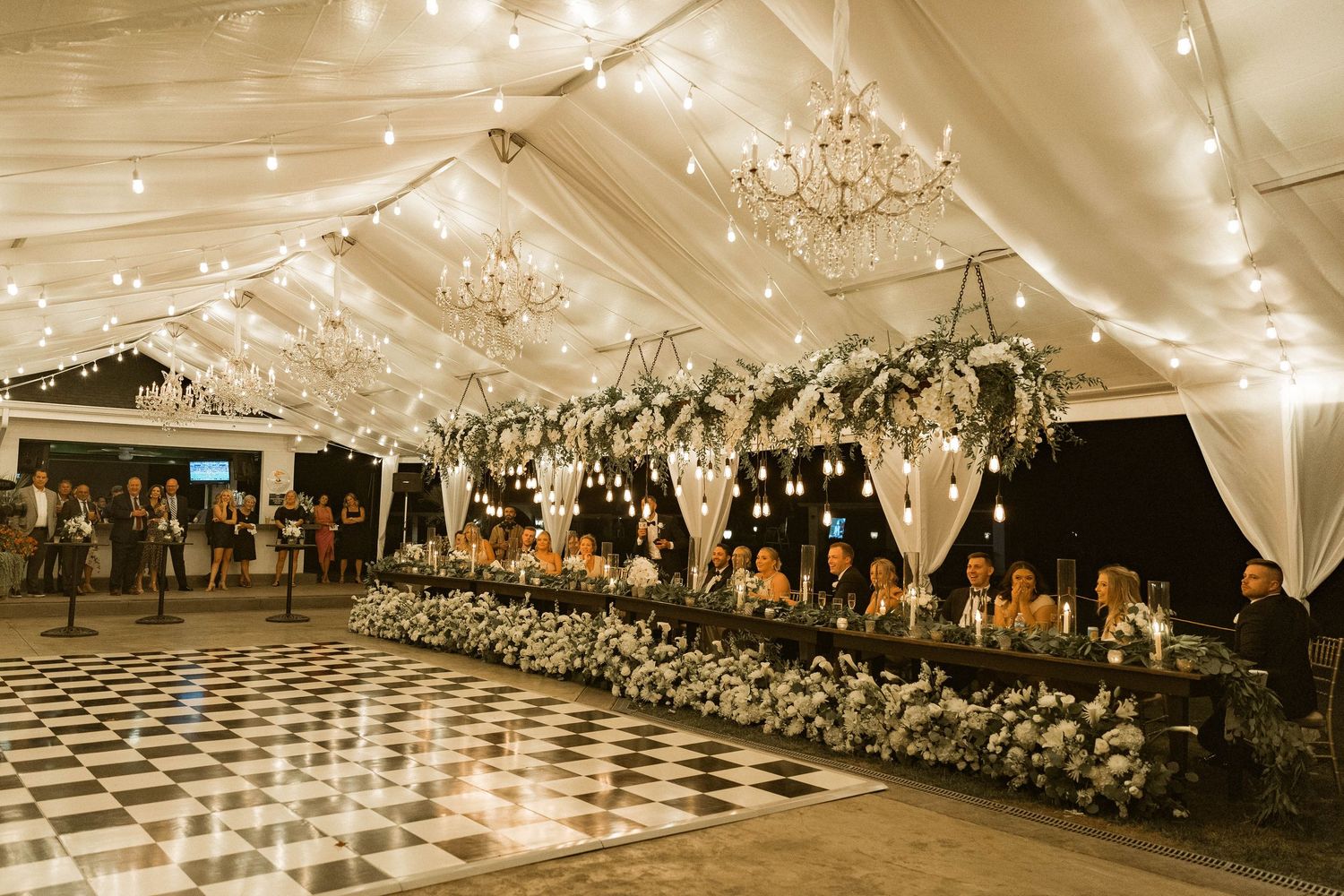 Elegant wedding reception tent with checkered floor and hanging floral arrangements.