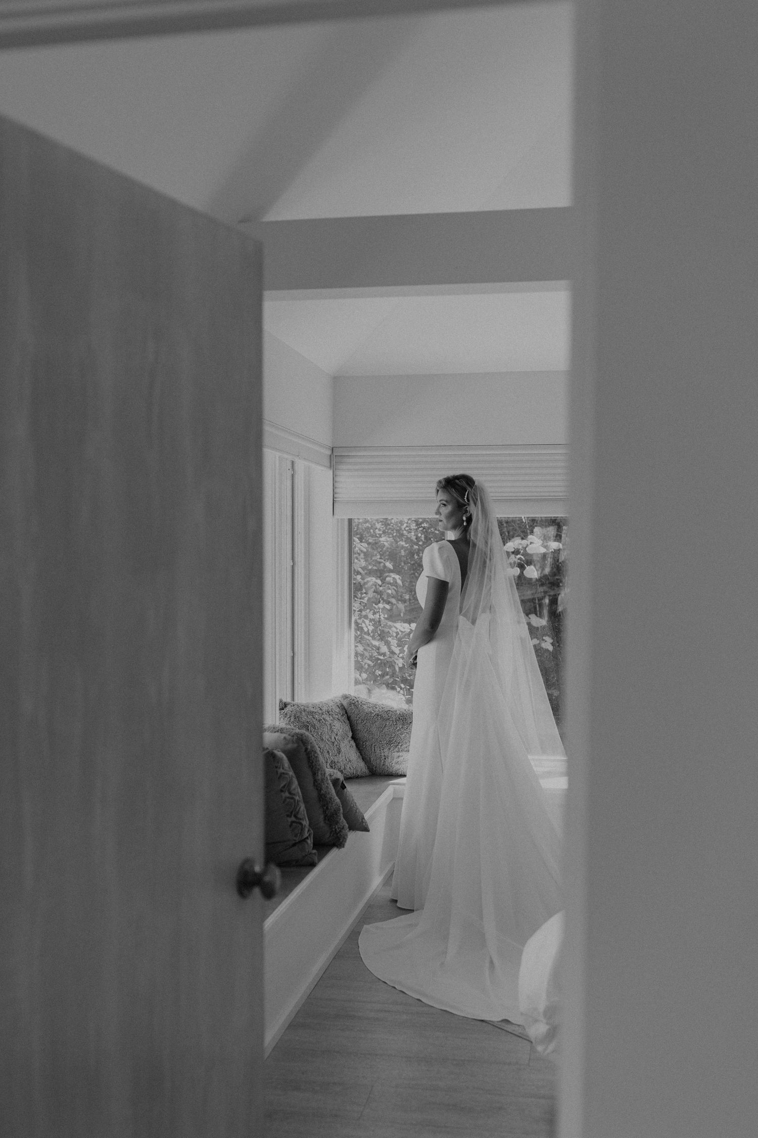 Wedding dress hanging in sunlit hallway creating dramatic silhouette.