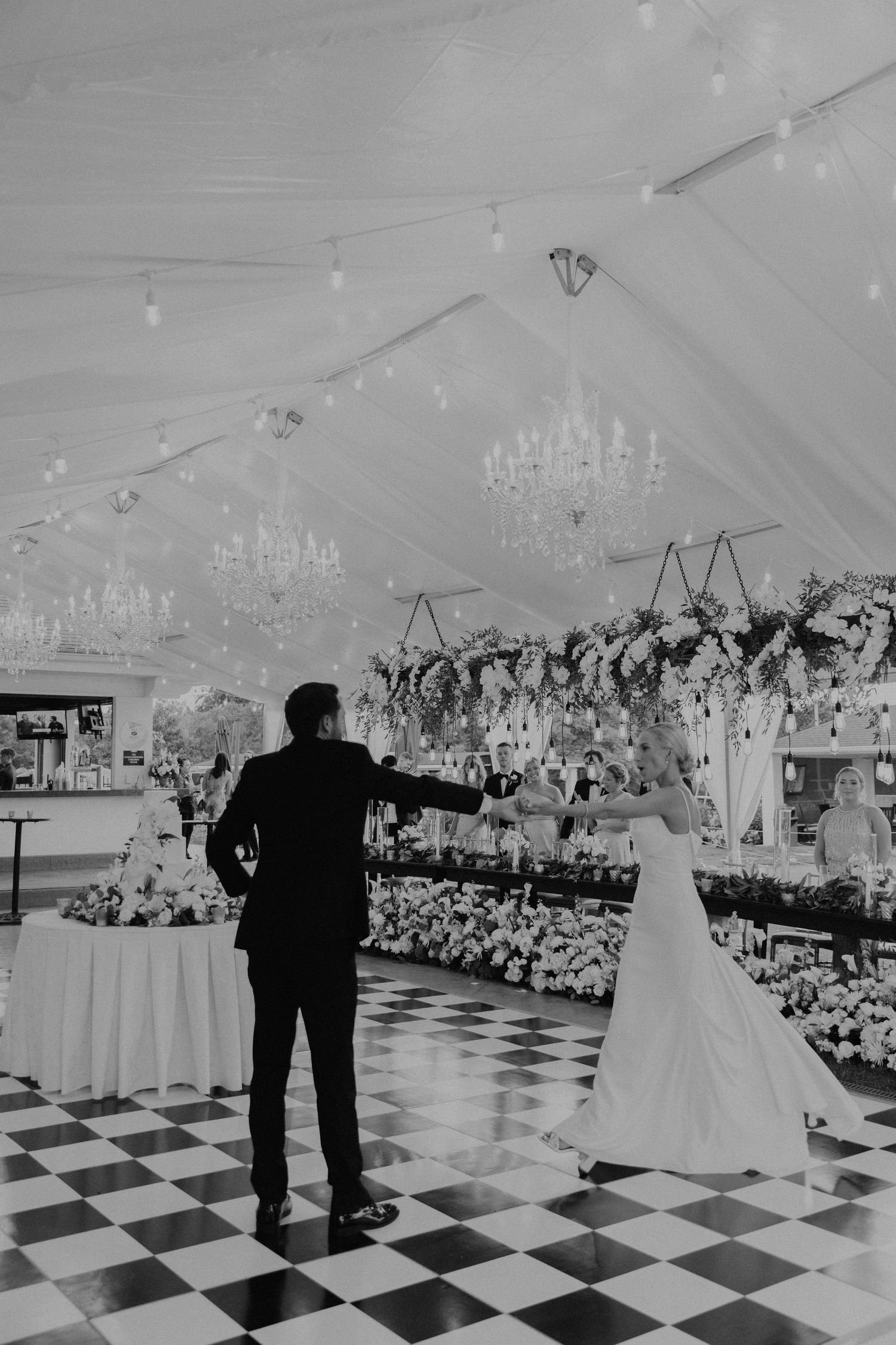 Black and white reception venue with checkered dance floor and elegant chandelier lighting.