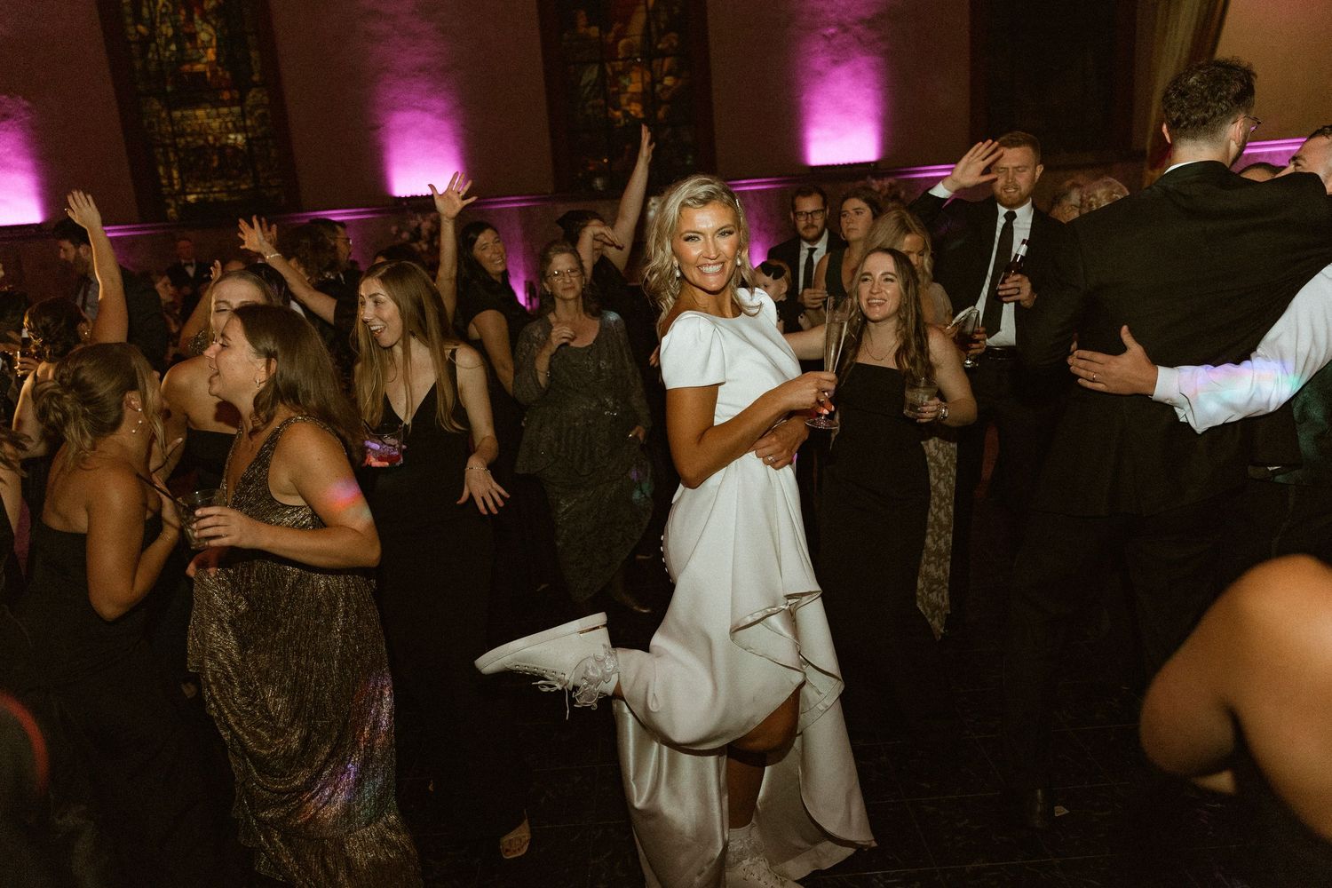 Wedding reception dance floor with party guests and pink ambient lighting.