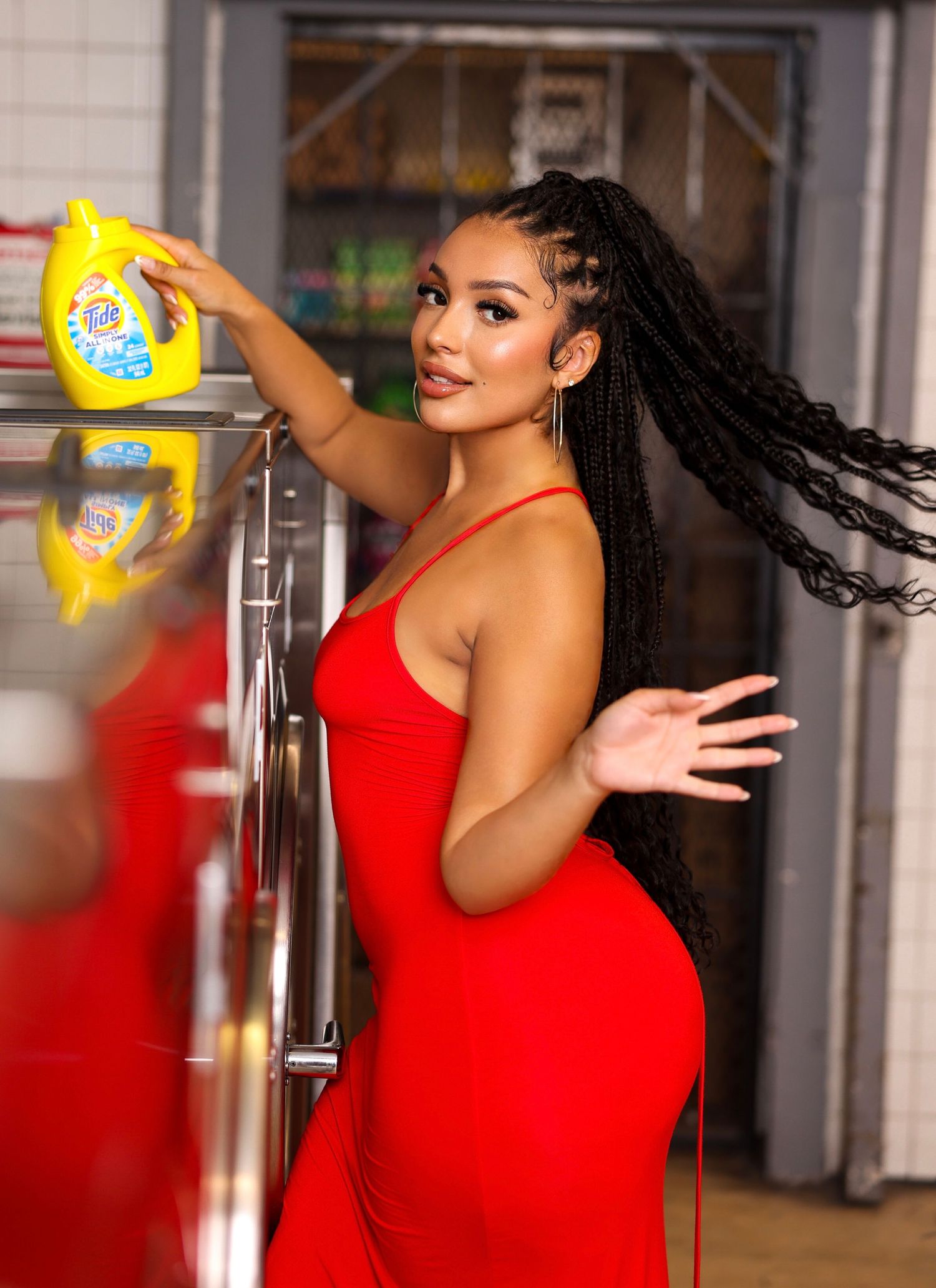 Woman in a vibrant red dress poses playfully with a yellow cup against an industrial background.