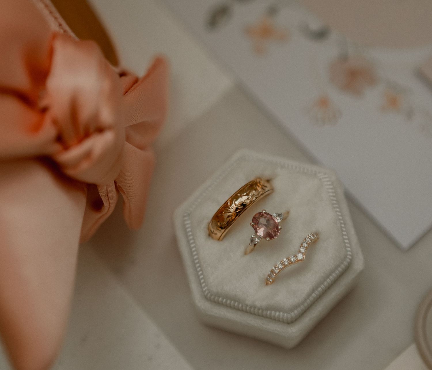 Delicate pink wedding details with white hexagonal ring boxes and soft floral decorations on a neutral background.