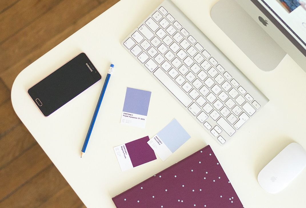 Minimalist desk workspace with Apple keyboard and scattered papers on white surface.