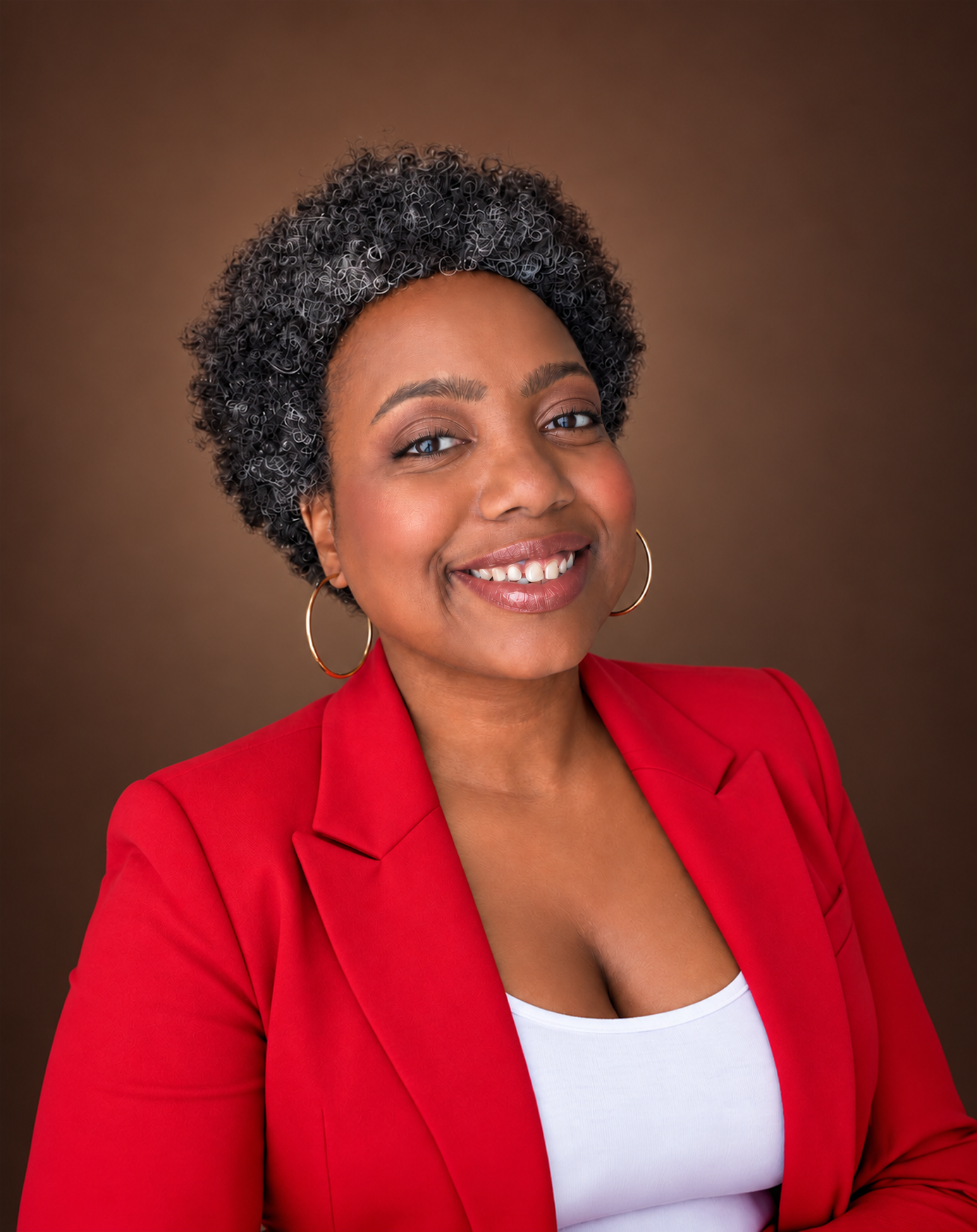 Smiling woman in red blazer and white top with hoop earrings, professional headshot on brown background.
