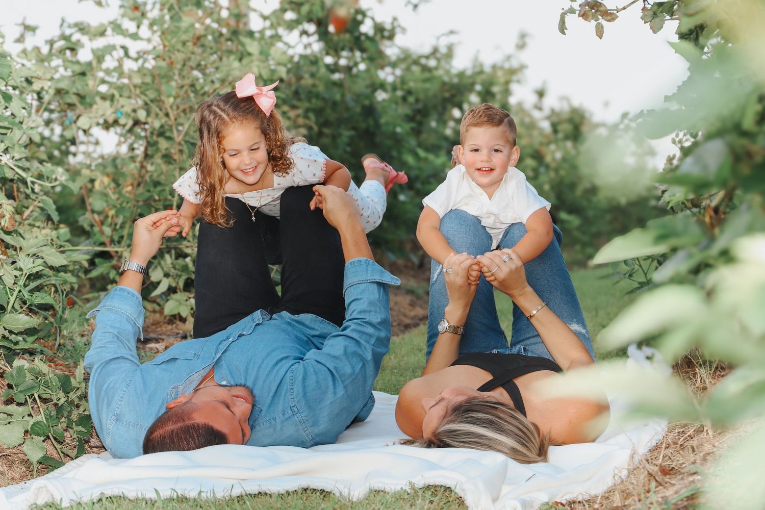 Joyful group playing and laughing together on a picnic blanket surrounded by greenery.