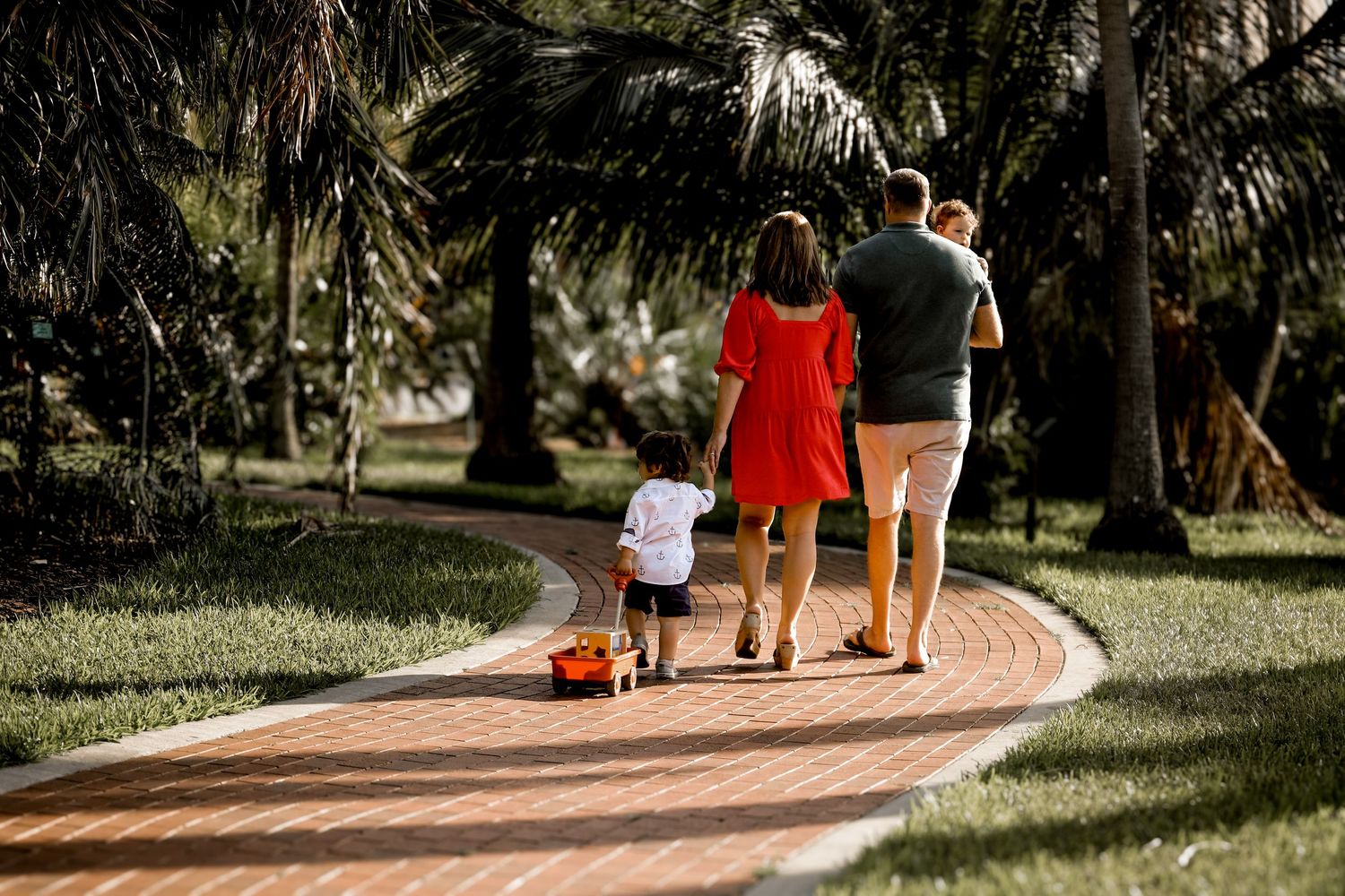 A family walks down a curved brick path together pulling a small red wagon.