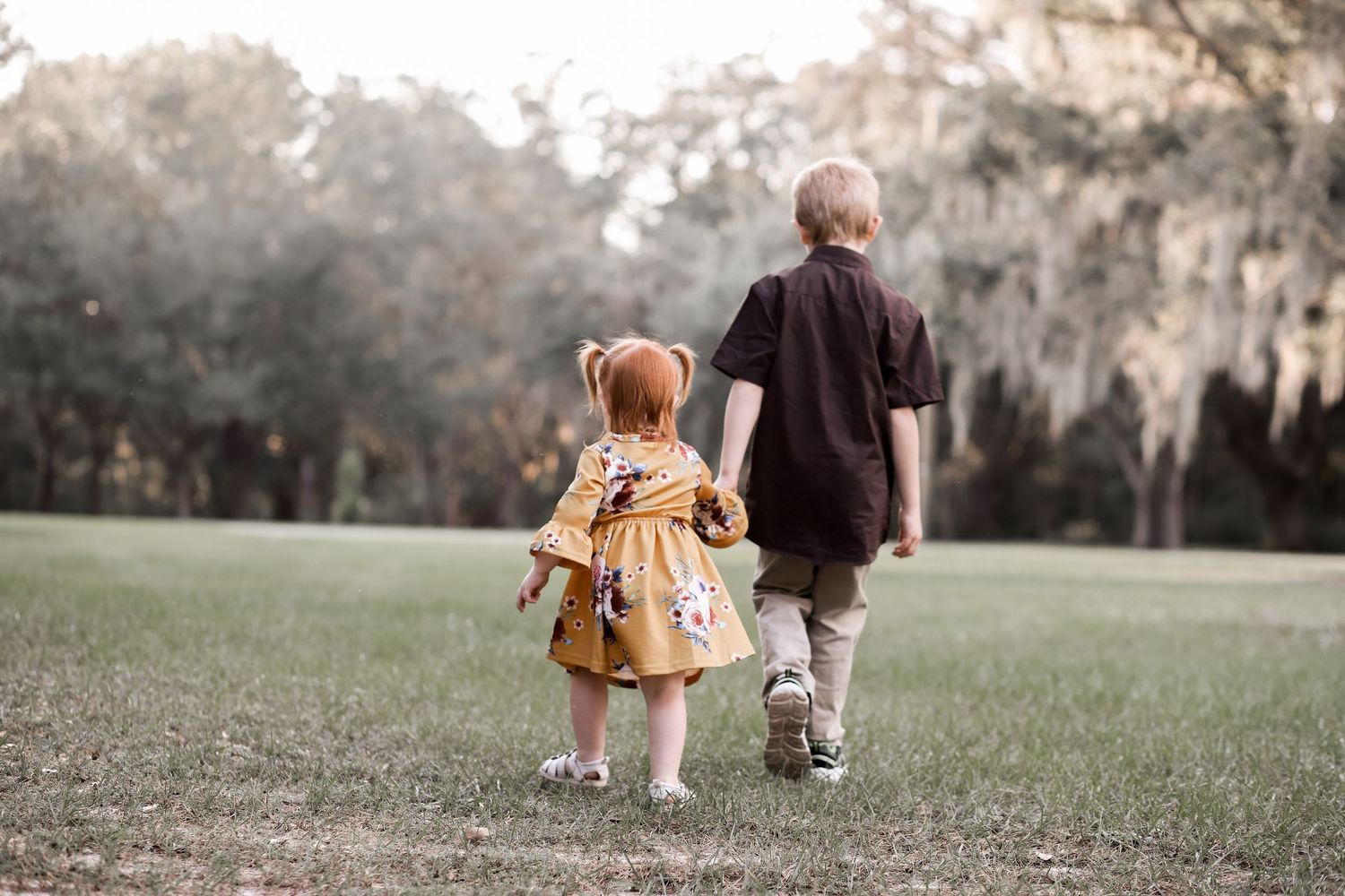 Parent and toddler holding hands walking together in a grassy field on an overcast day.
