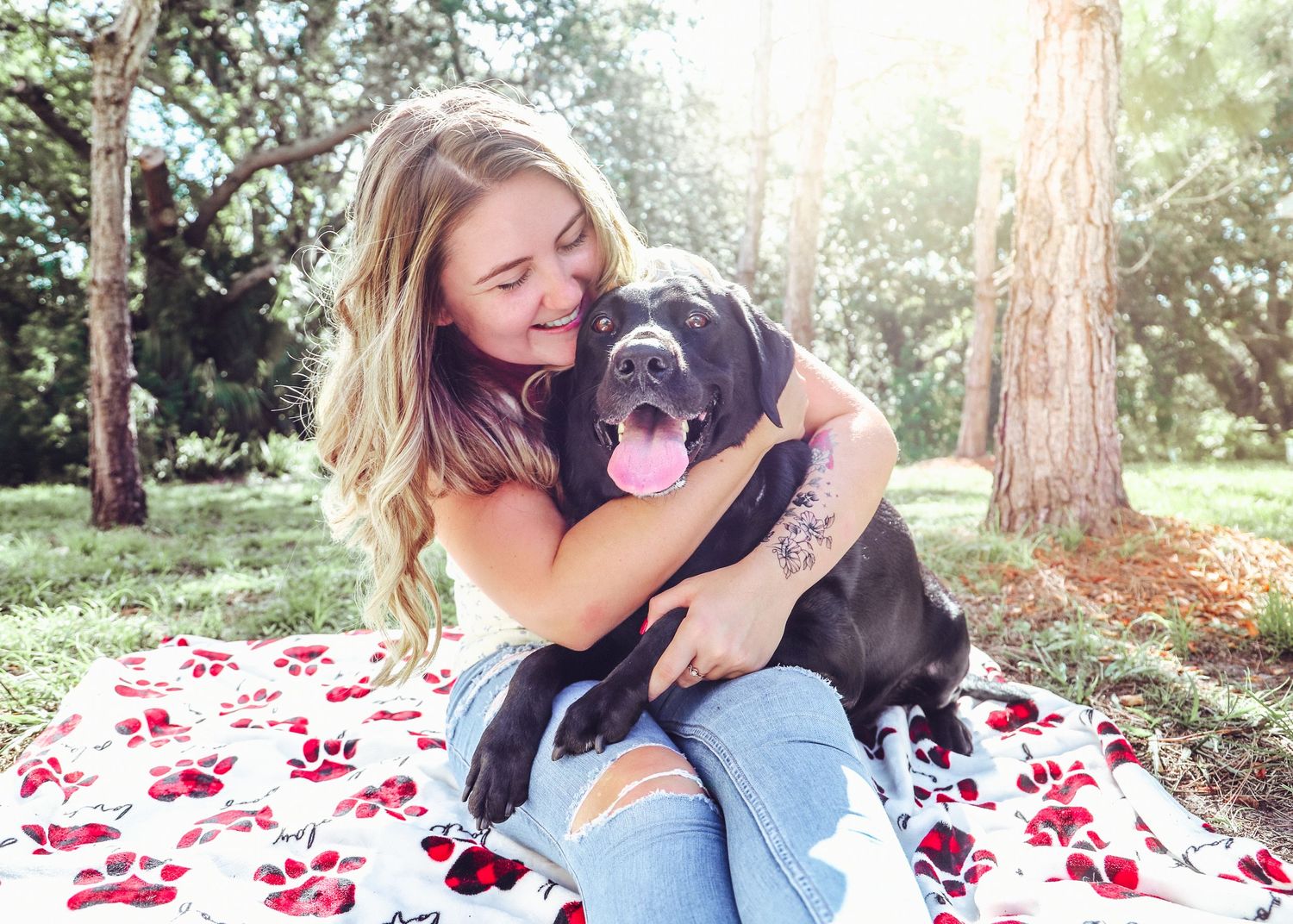 Candid moment of black dog and companion cuddling on patterned blanket in park setting.