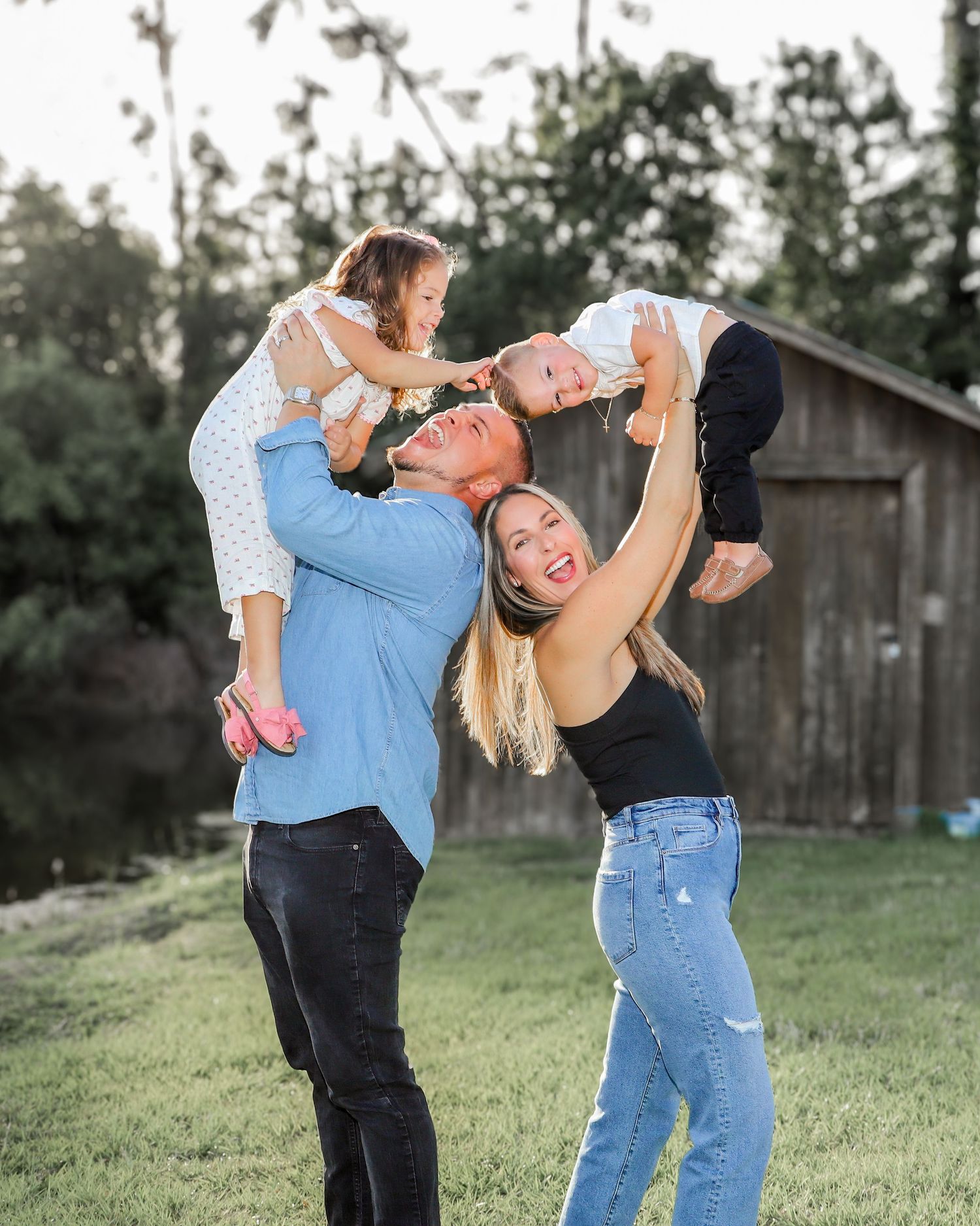 Candid family moments captured in a green field with rustic barn in background.