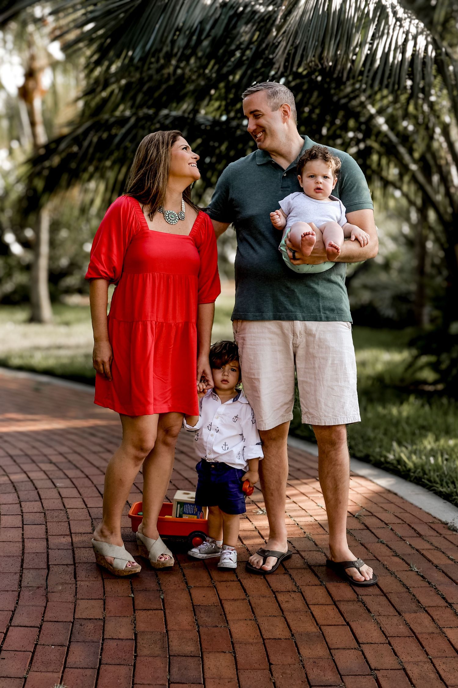 A cheerful family shares laughs while posing together on a brick pathway in a tropical setting.