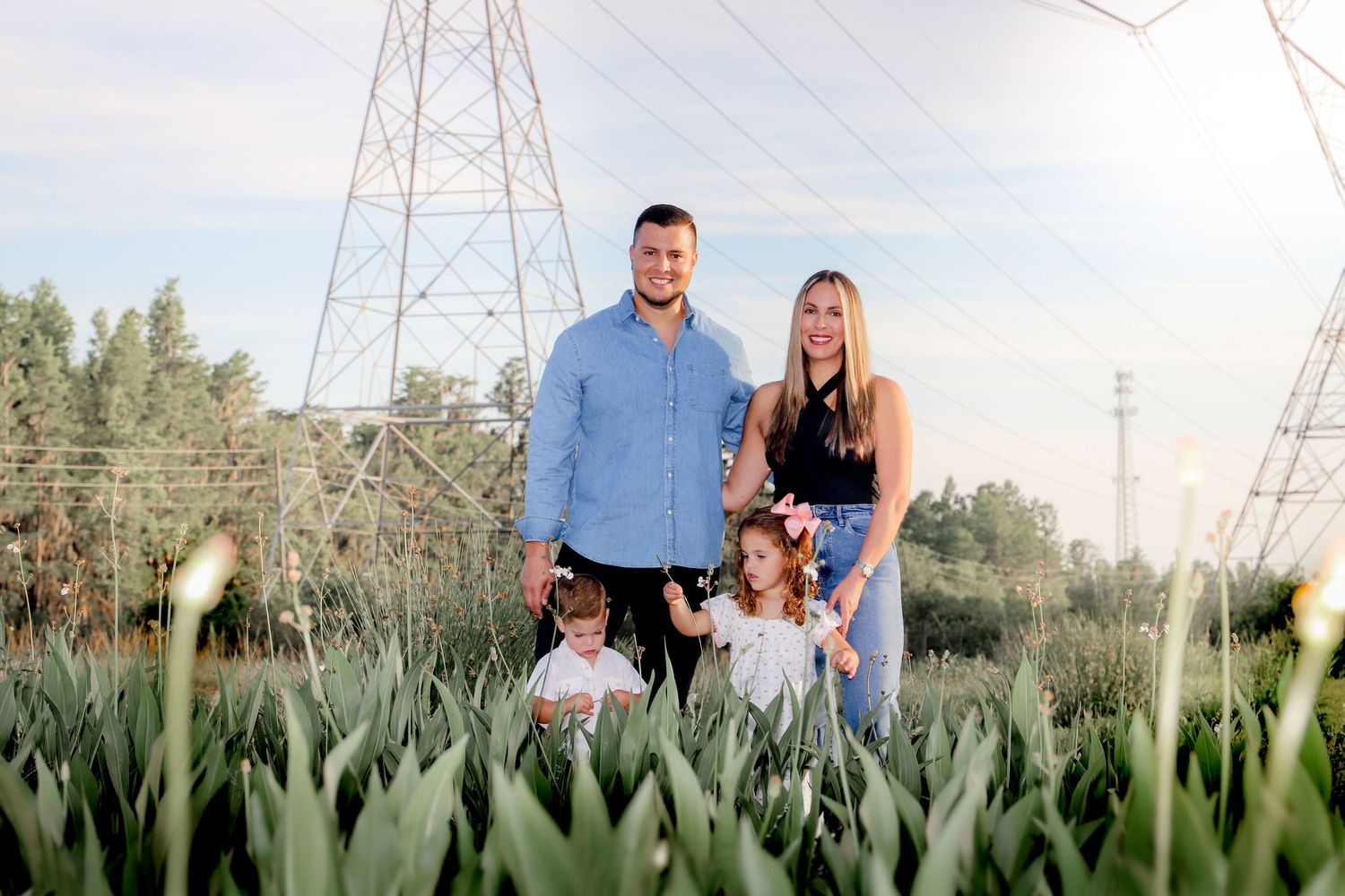 Family standing together in tall grass field with power lines overhead.