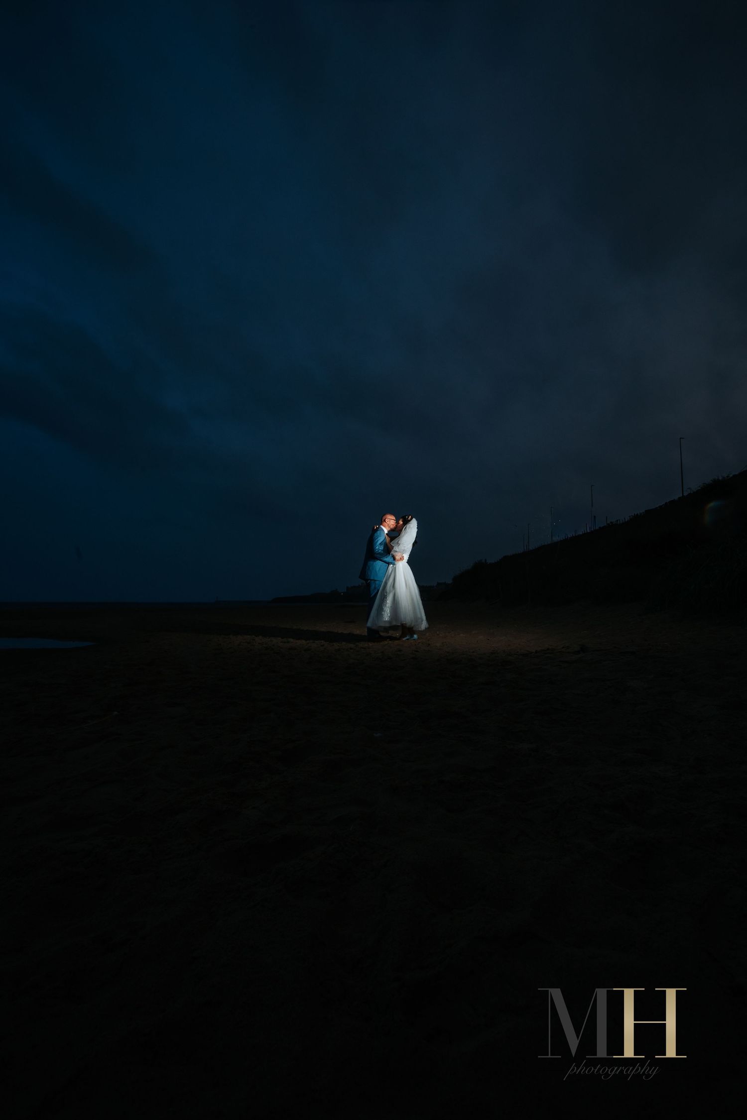Dramatic nighttime silhouette of wedding couple illuminated against dark landscape.