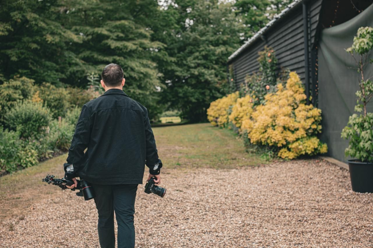 A couple walks along a gravel garden path surrounded by lush greenery and yellow flowers.