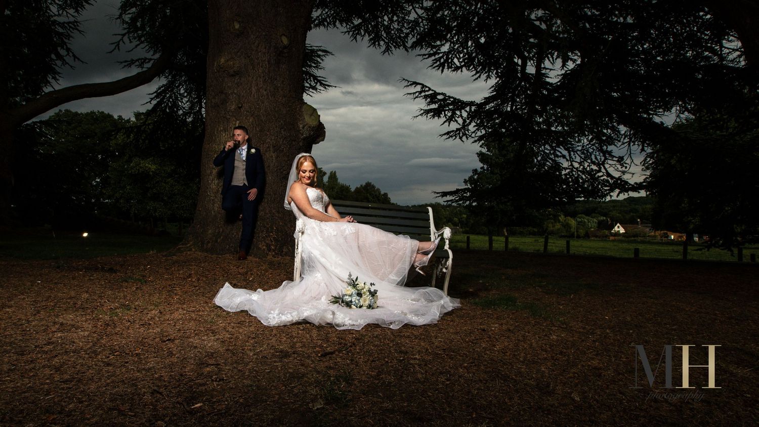 Wedding couple walking through autumn leaves under tall trees at dusk.