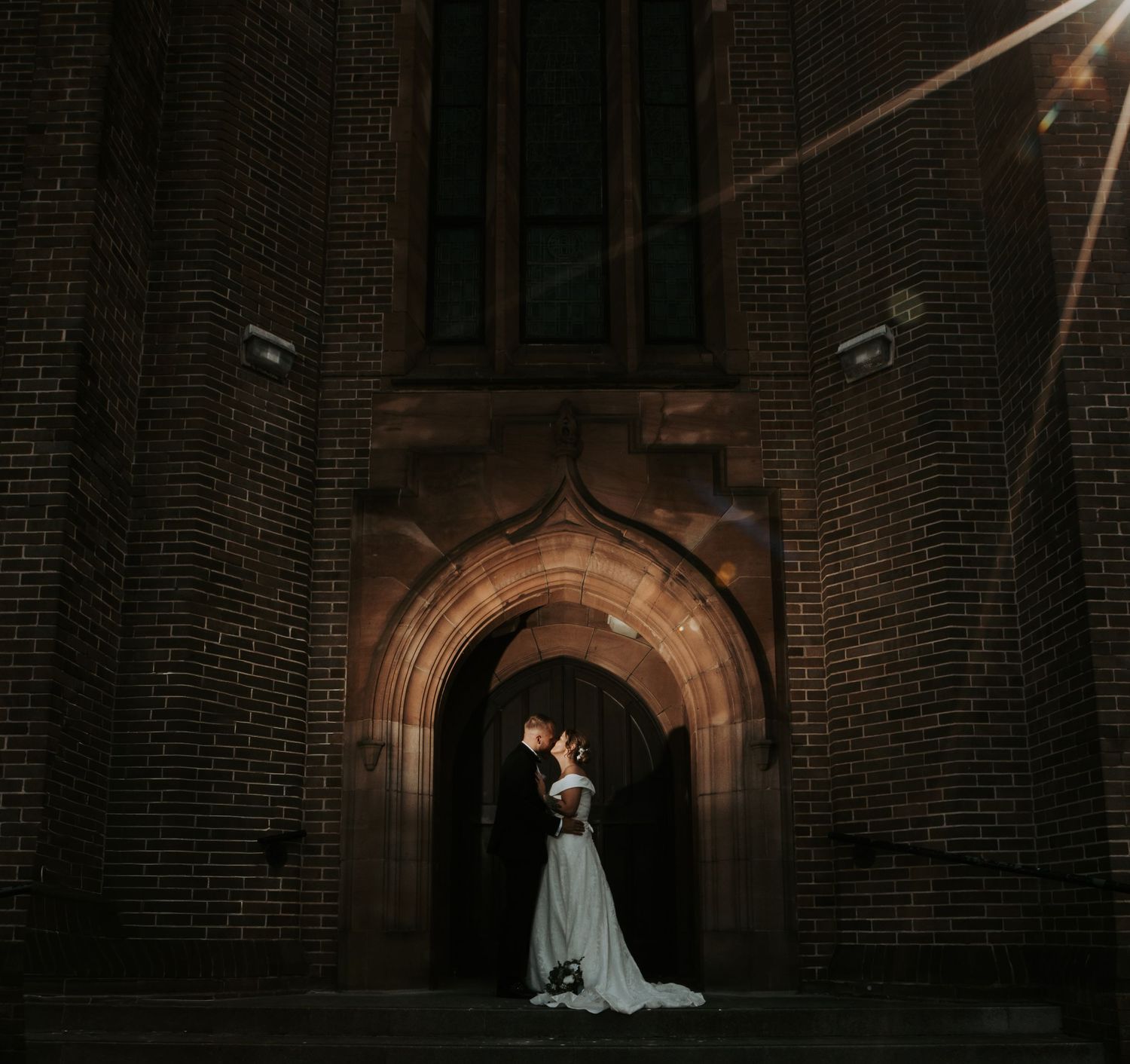 A dramatic wedding photo series showing a couple in silhouette against arched brick doorways in a dark corridor.