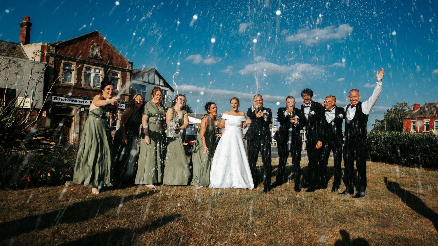 Wedding celebration panorama with bridal party posing against bright blue winter sky.