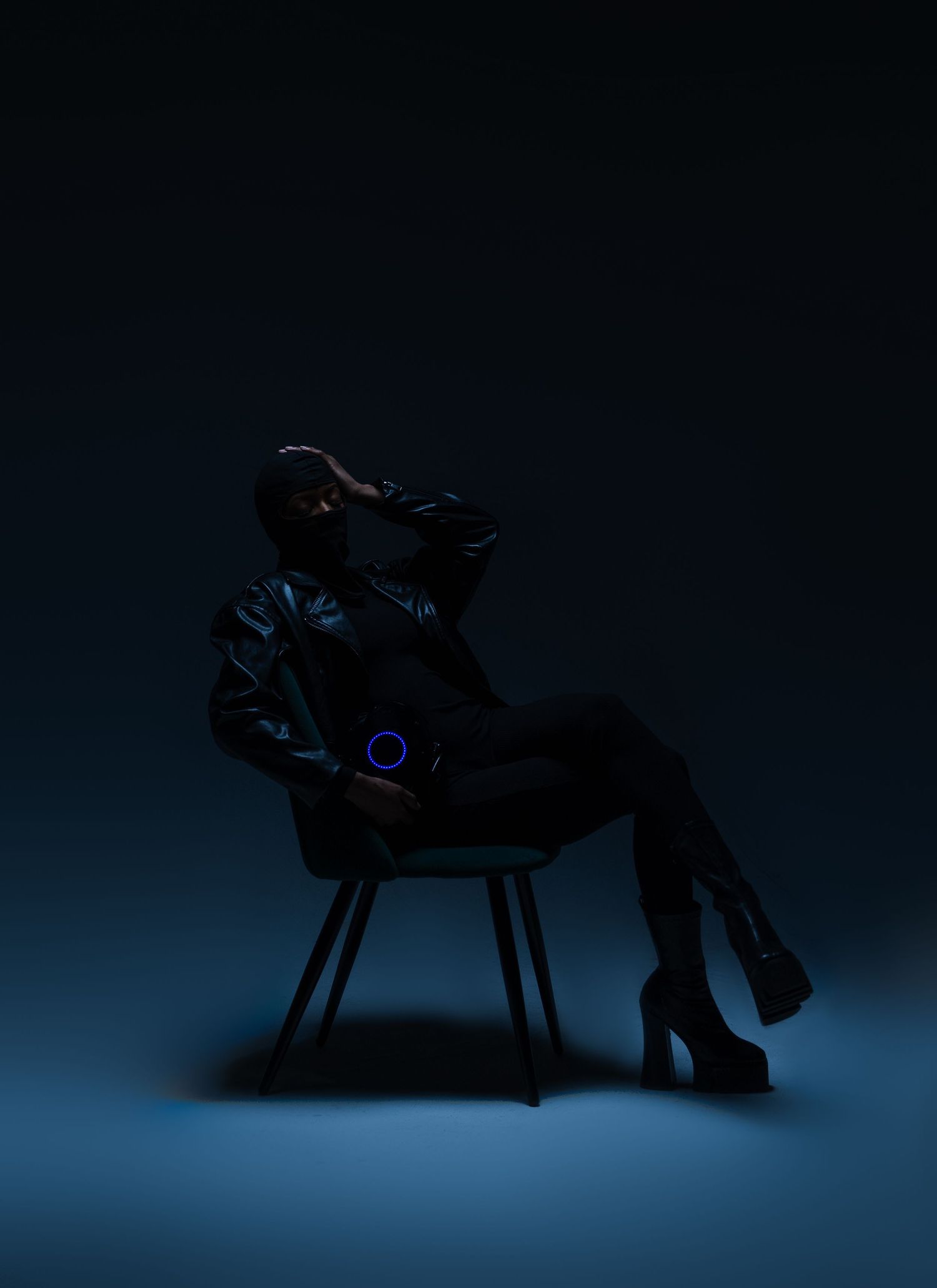 Moody silhouette of figure seated in chair with glowing ring accent against dark blue background.