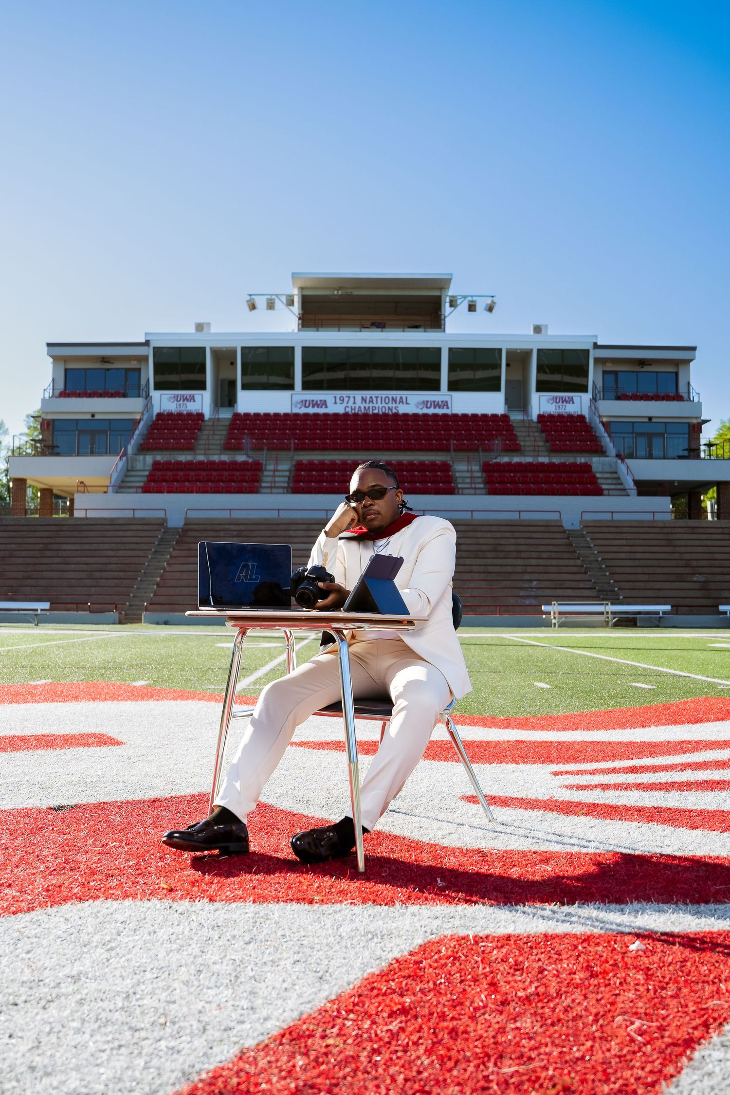 Professional photoshoot setup on a red and white stadium field under bright blue sky.