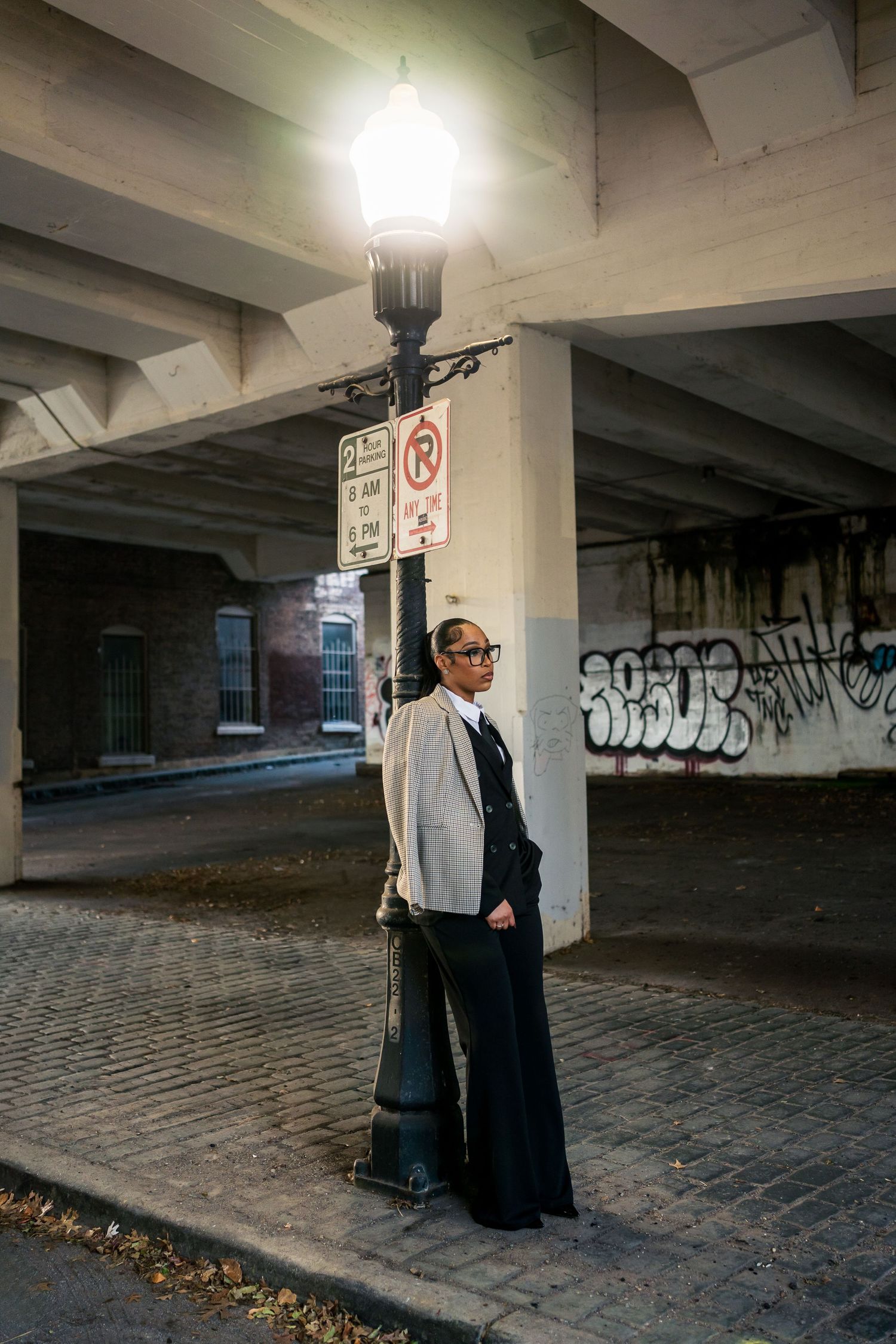 A couple stands together in a dimly lit parking garage with graffiti-covered walls and cobblestone flooring.