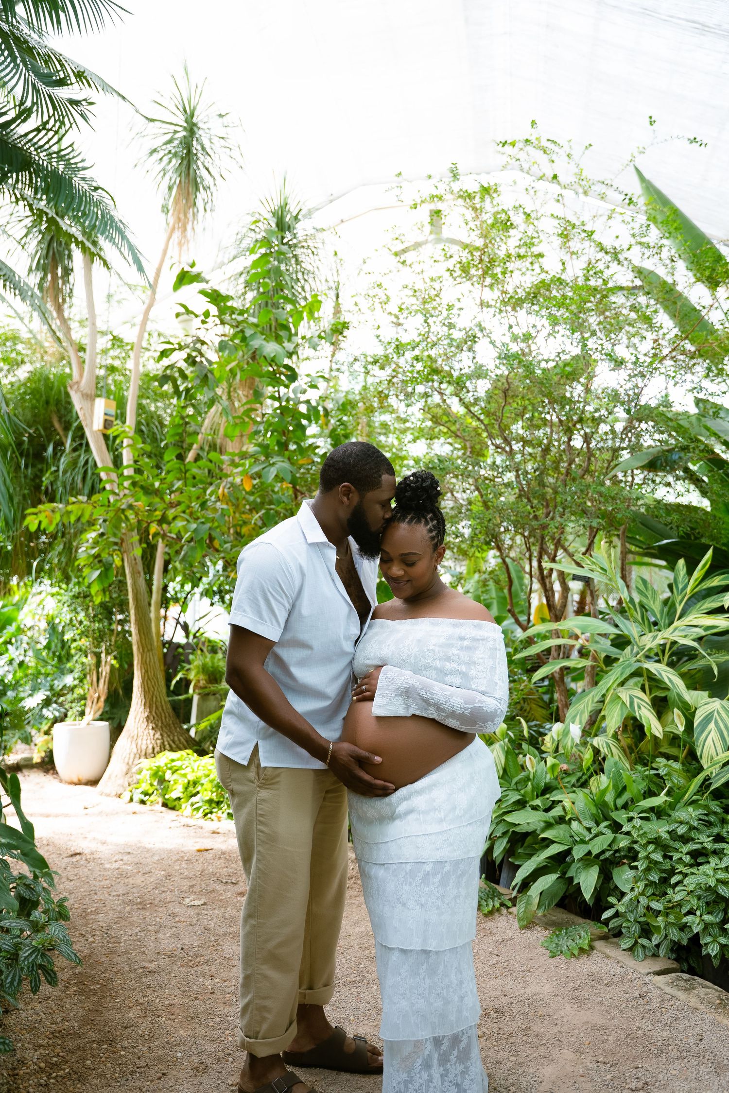 A tender maternity moment captured in a greenhouse setting with tropical plants.