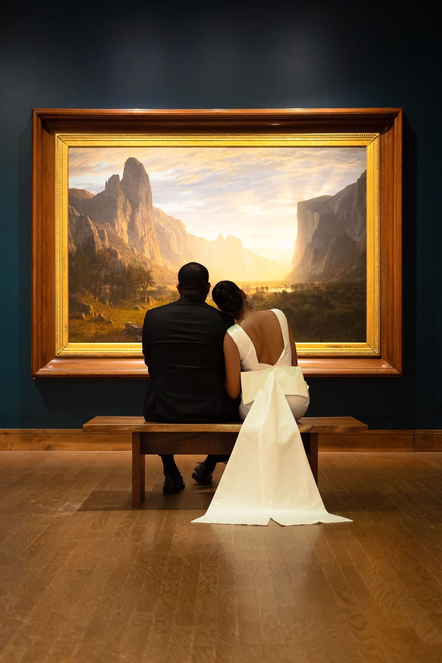 Silhouette of newlyweds viewing dramatic landscape painting in museum gallery.