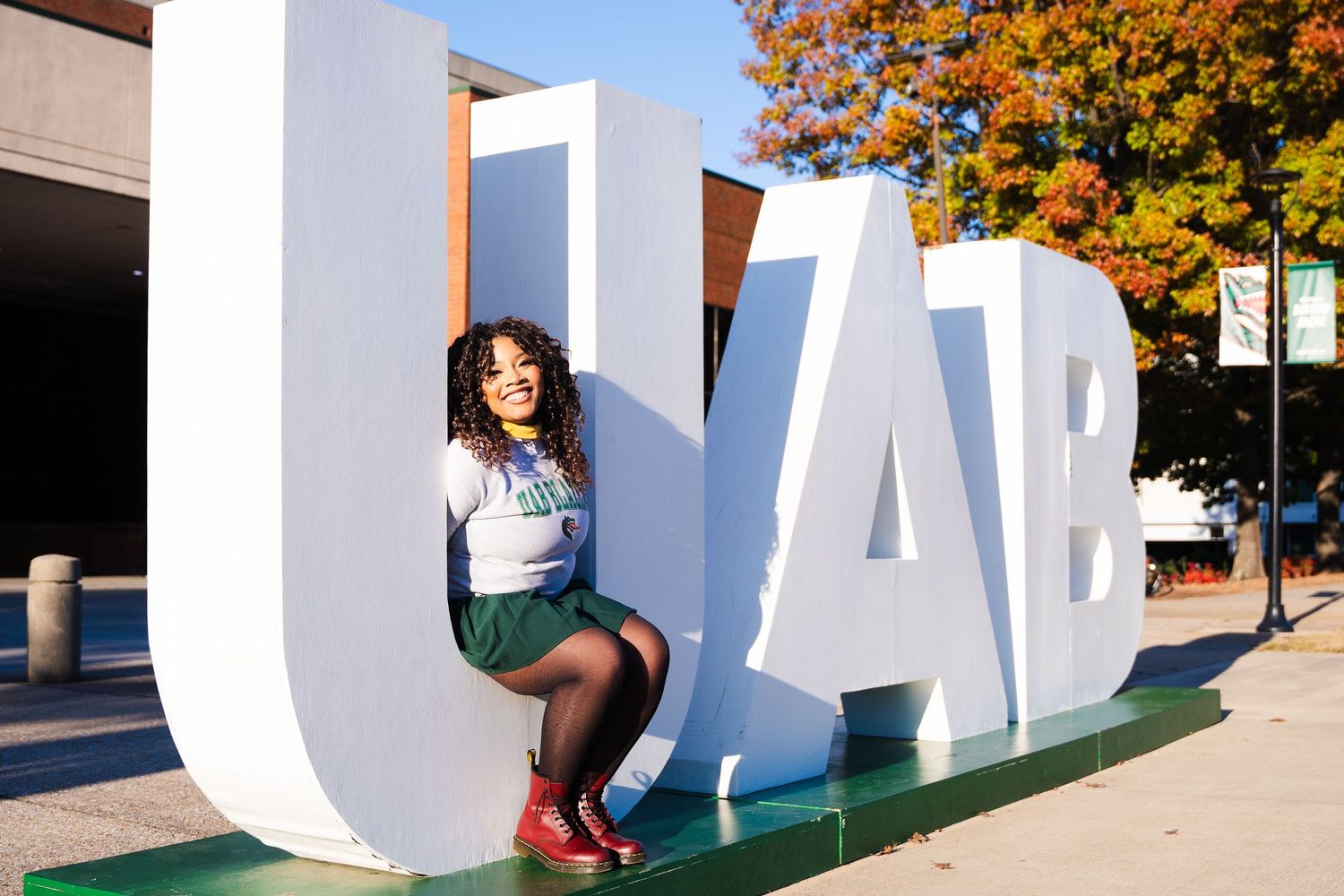 Graduate poses on large UAB outdoor letters during autumn season.