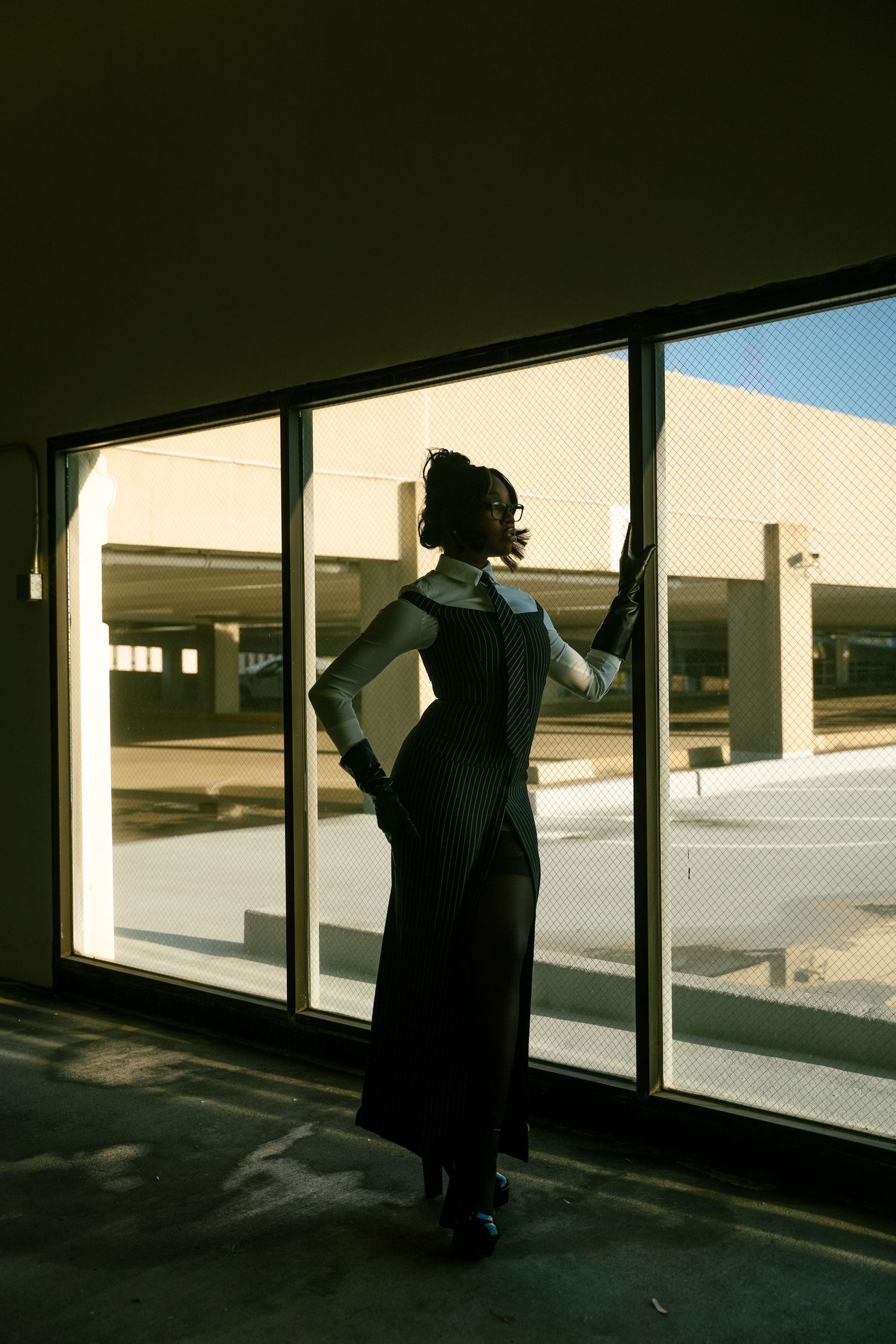Silhouette figure stands against bright windows in an empty room creating dramatic light and shadow contrast.