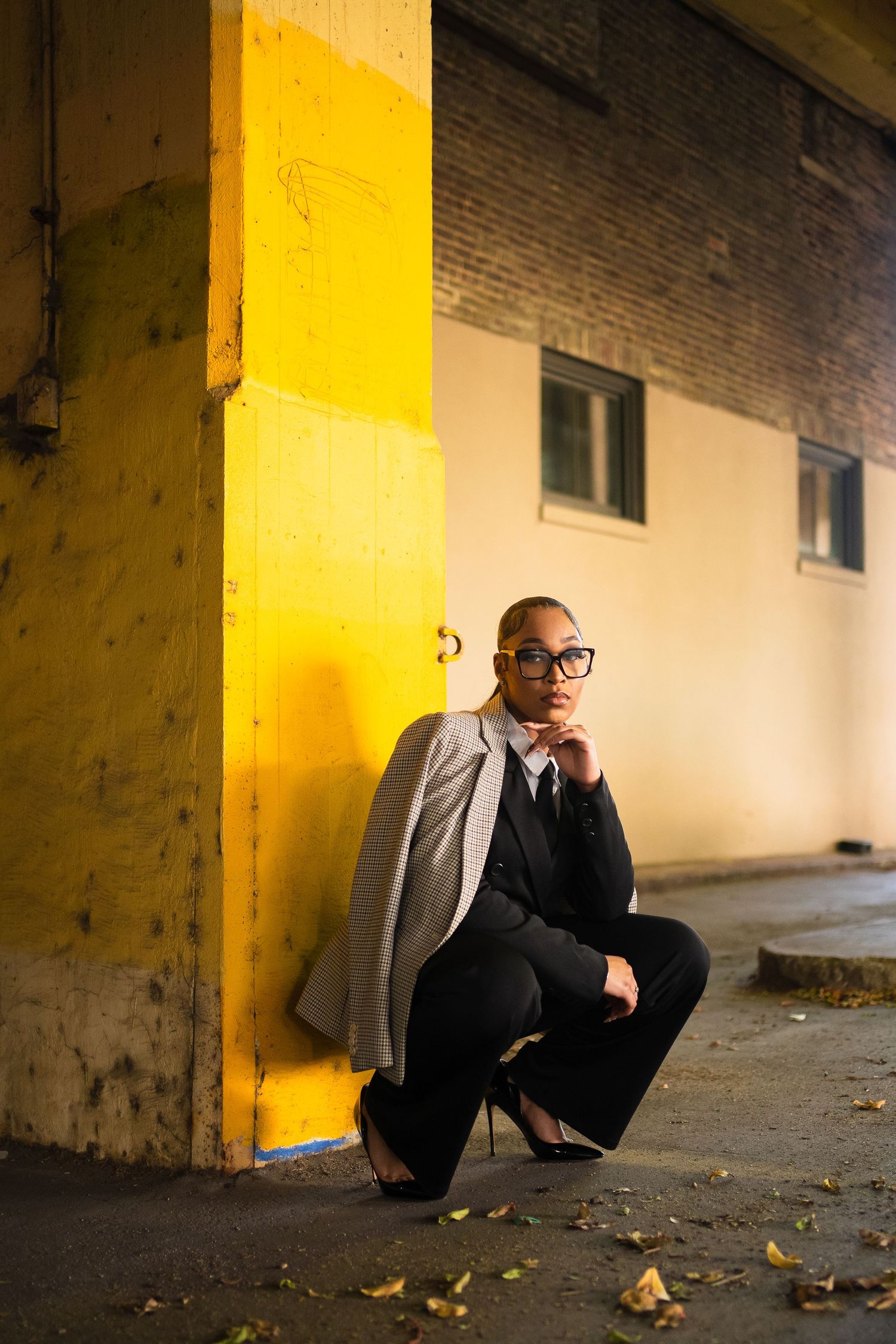 A person in a suit crouches in a dimly lit hallway with yellow lighting and scattered leaves on the ground.