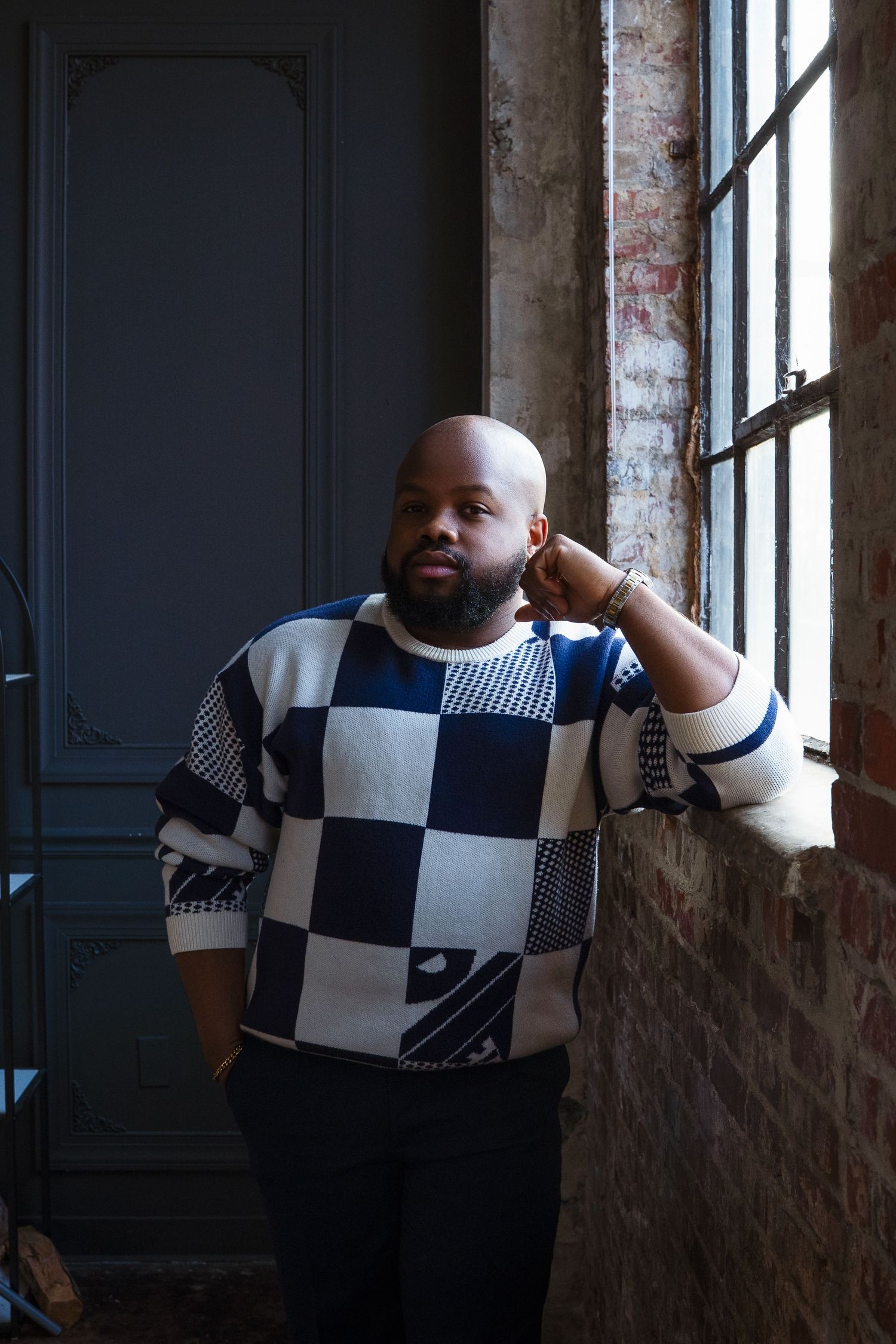 A creative portrait against brick wall featuring a black and white checkered sweater outfit.