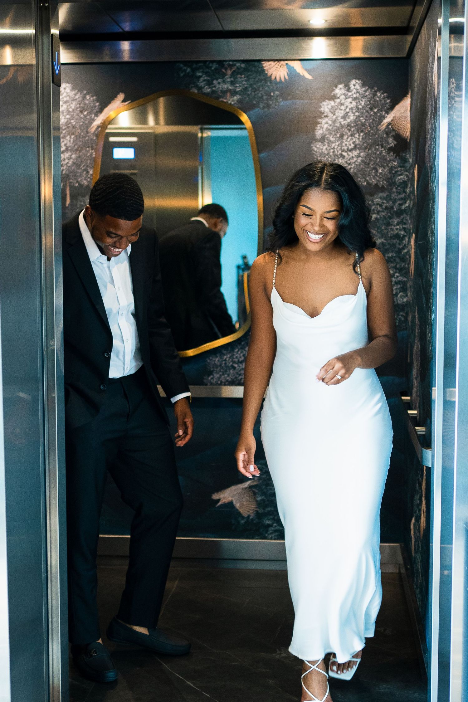 A couple sharing a joyful moment while exiting an elevator in formal wear.