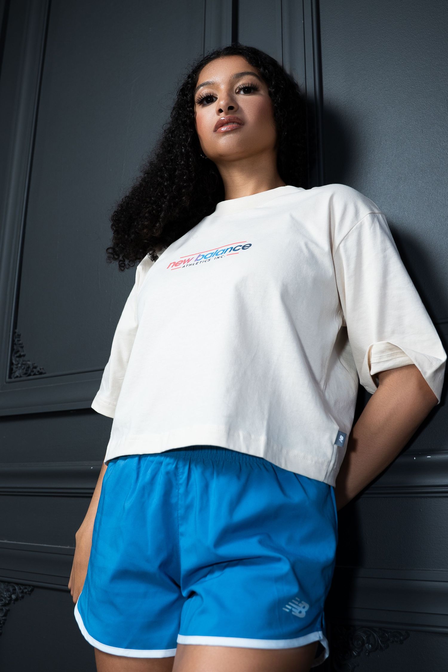Sporty outfit combination with white crop top and bright blue athletic shorts against dark wall.