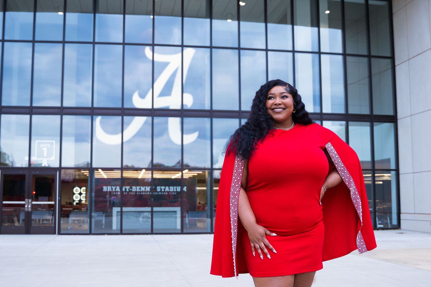 Person in vibrant red cape dress posing confidently in front of a modern building with large windows.