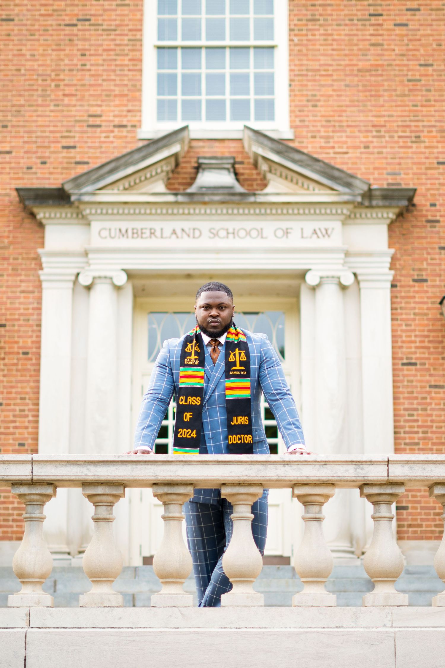 Law school graduate in academic regalia posing at Cumberland School of Law entrance.