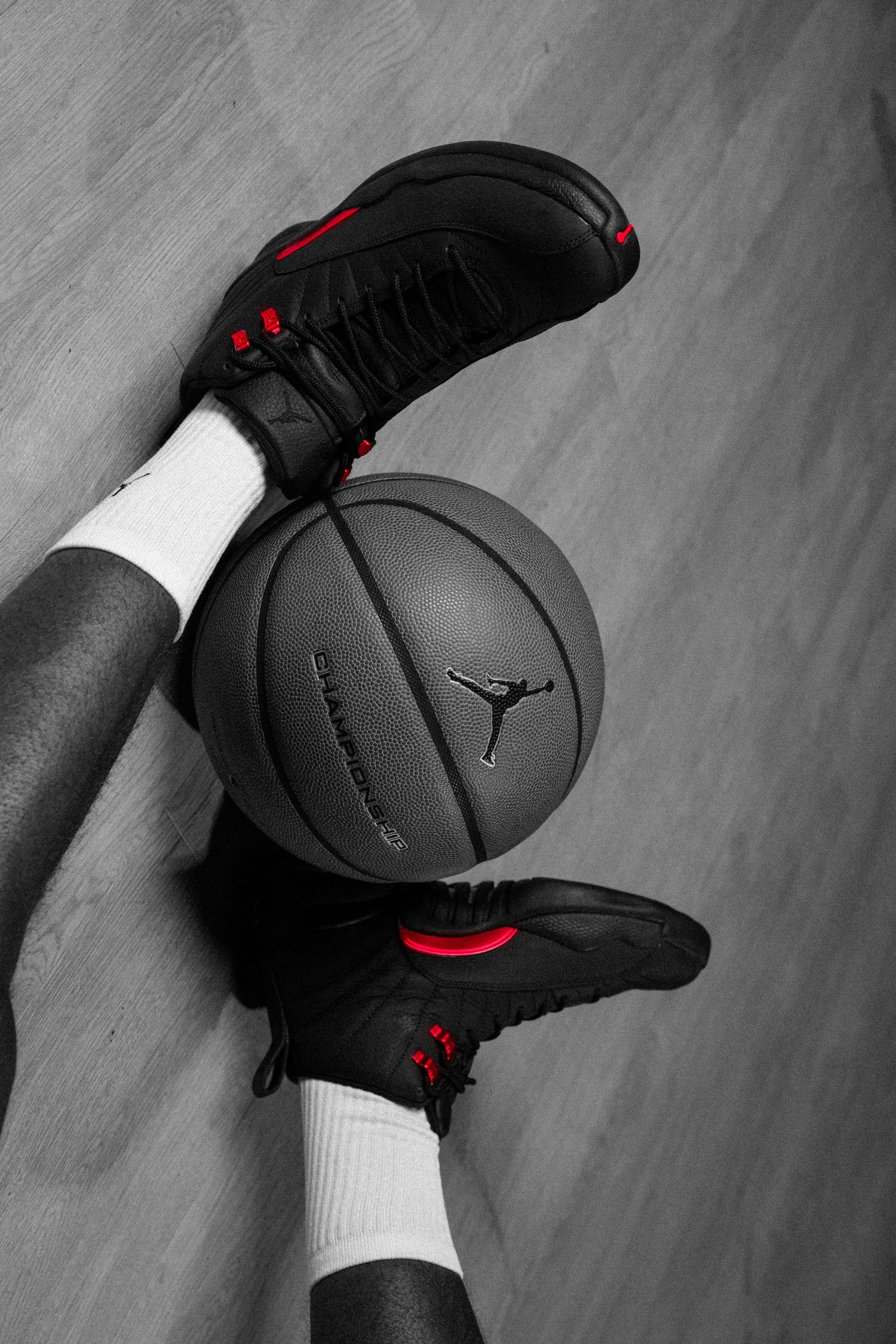 Black and red Air Jordan sneakers gripping a dark basketball on a hardwood court floor.