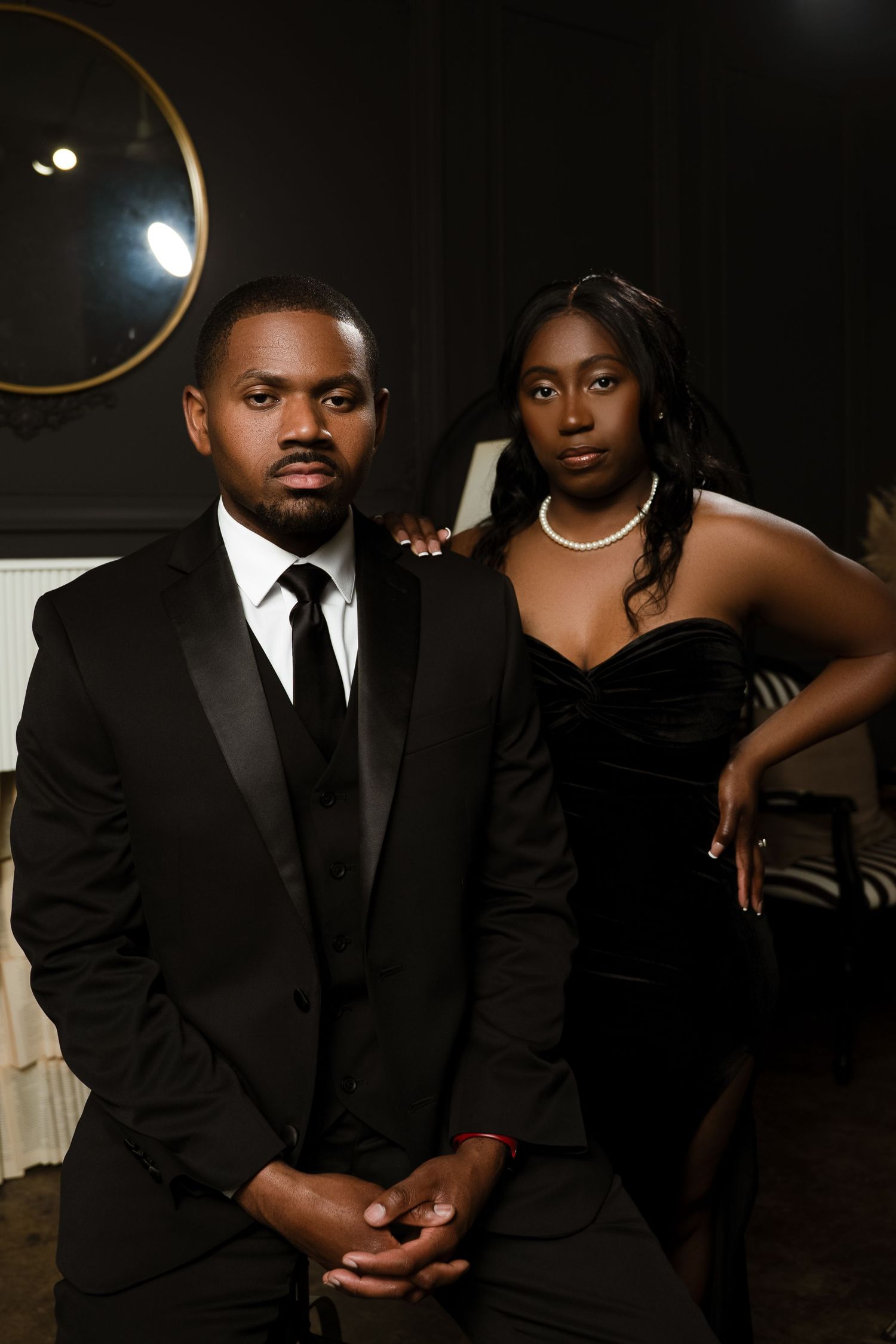 A formal portrait of a couple in black evening wear against a dark background.